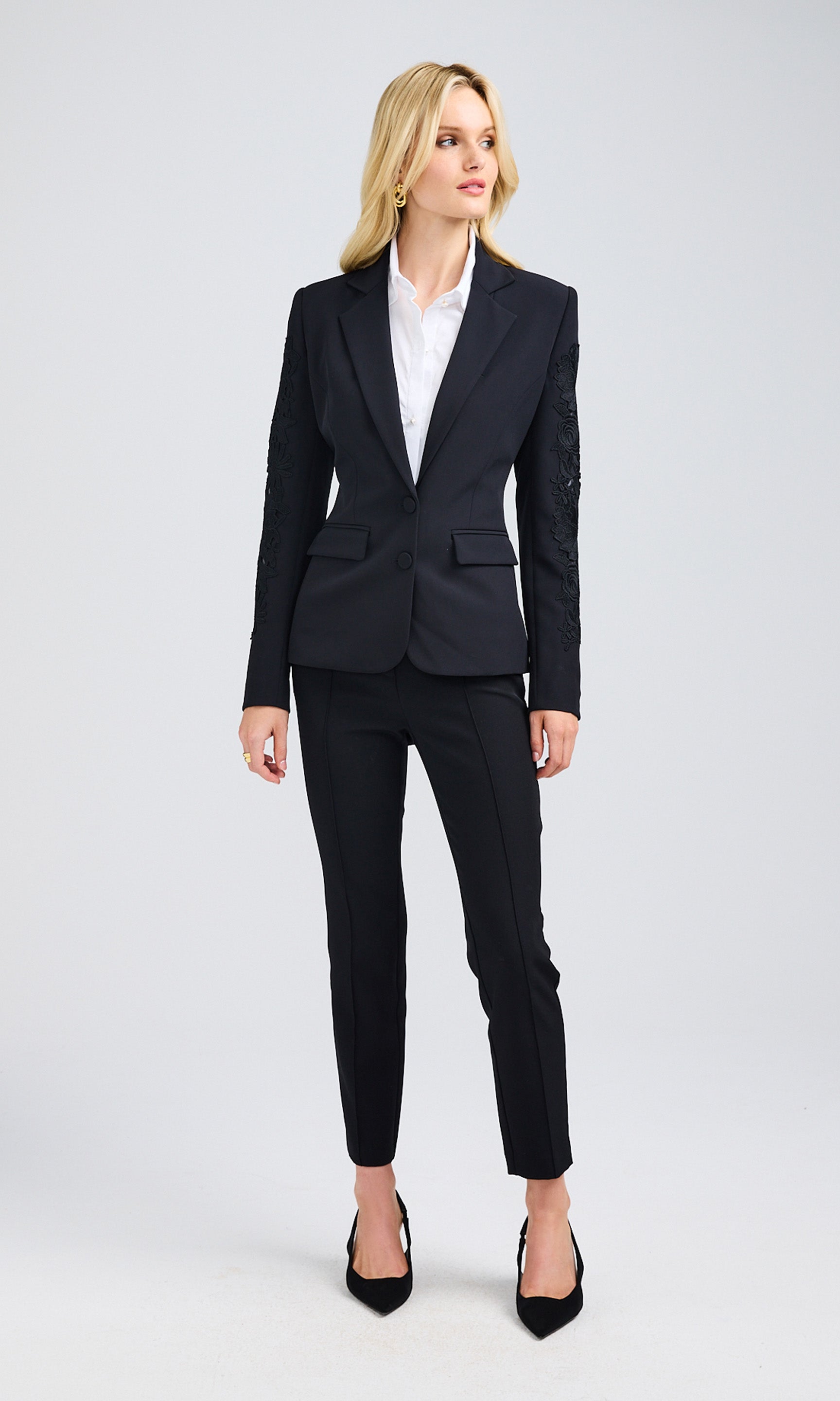 Woman wearing a black lace-combo blazer over a white blouse and paired with black crepe pants.