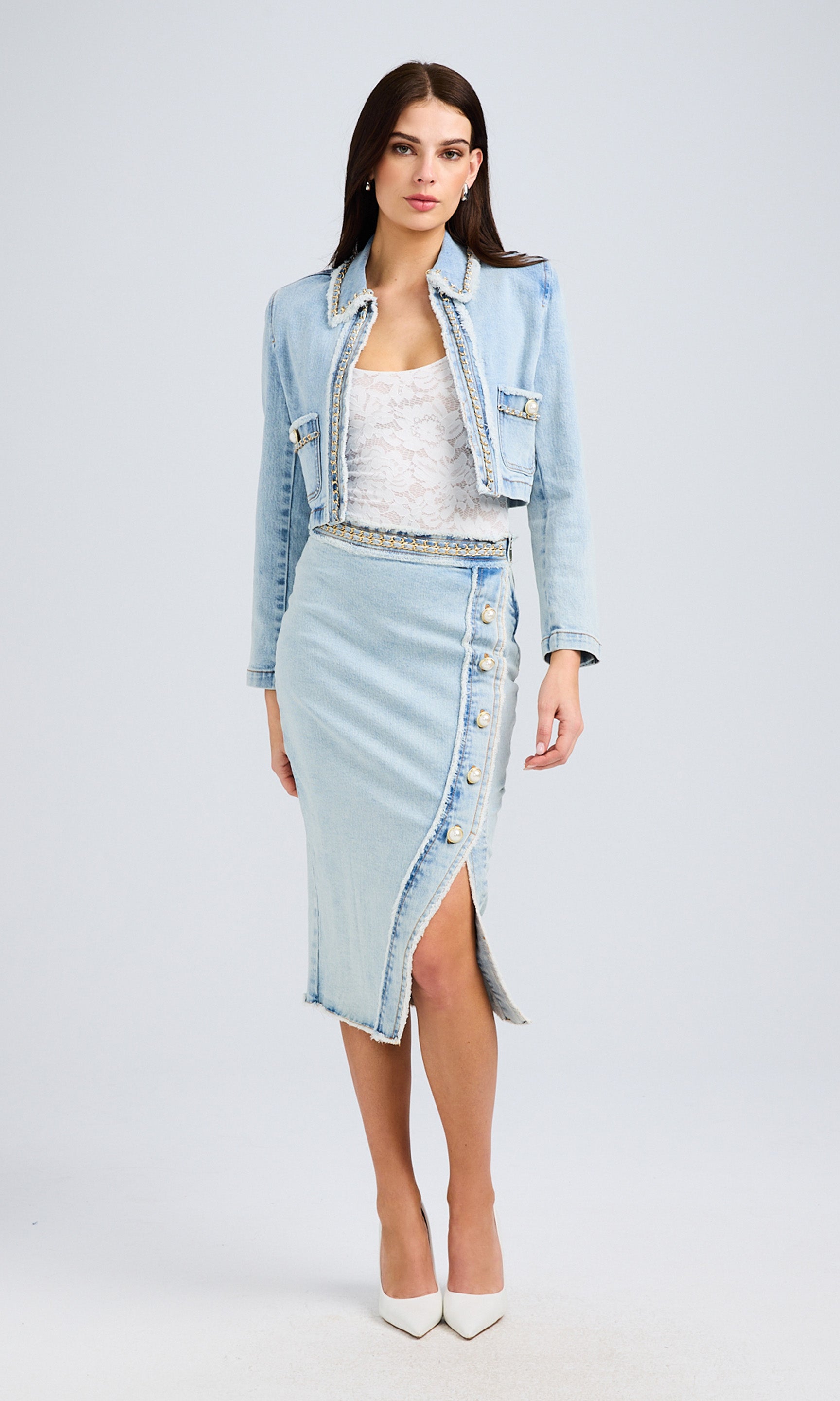 Full-body view of a model in a denim jacket and high-slit skirt, paired with a white top and heels.