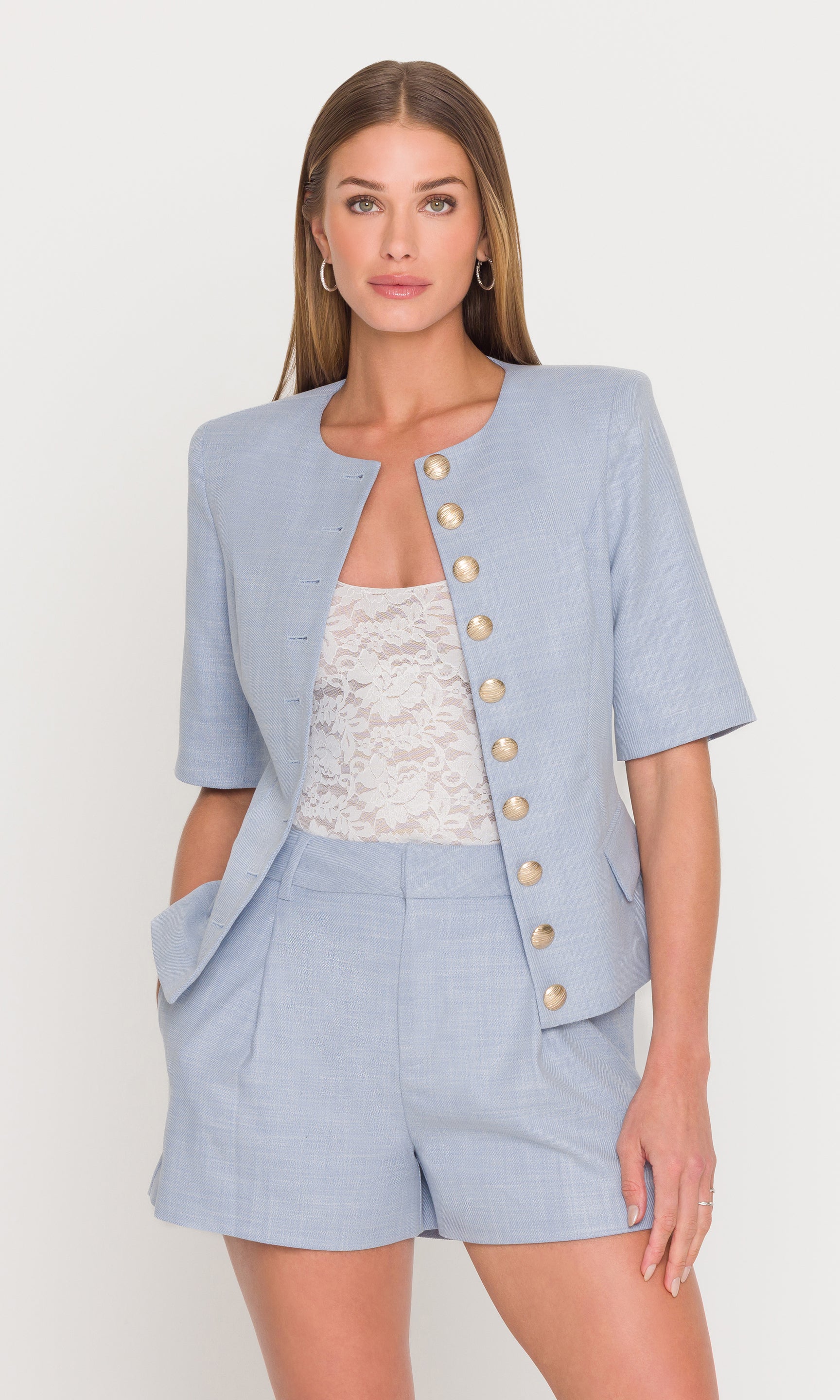 Model wears the Adriana Chambray Suiting Jacket in chambray blue styled open over a lace top with matching shorts in a front view, showing the polished set look.