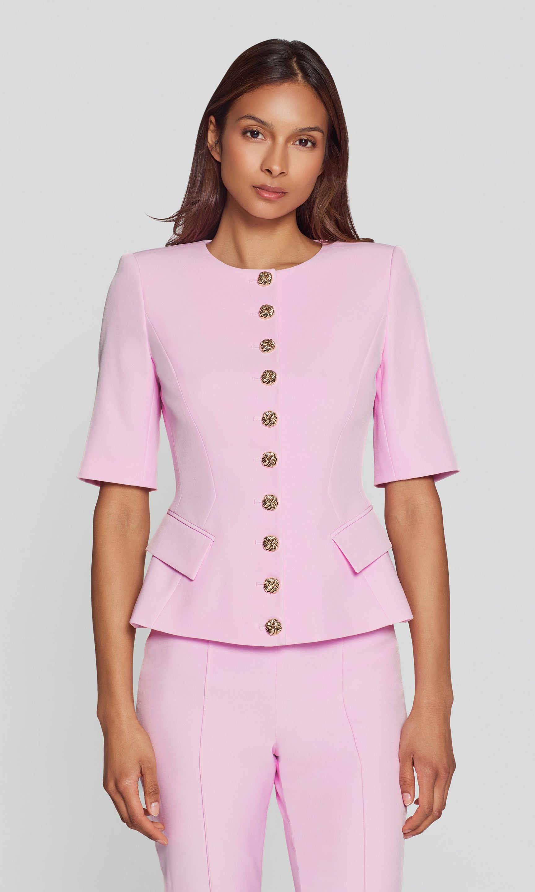Woman wearing a pink suit with gold buttons on a light gray background