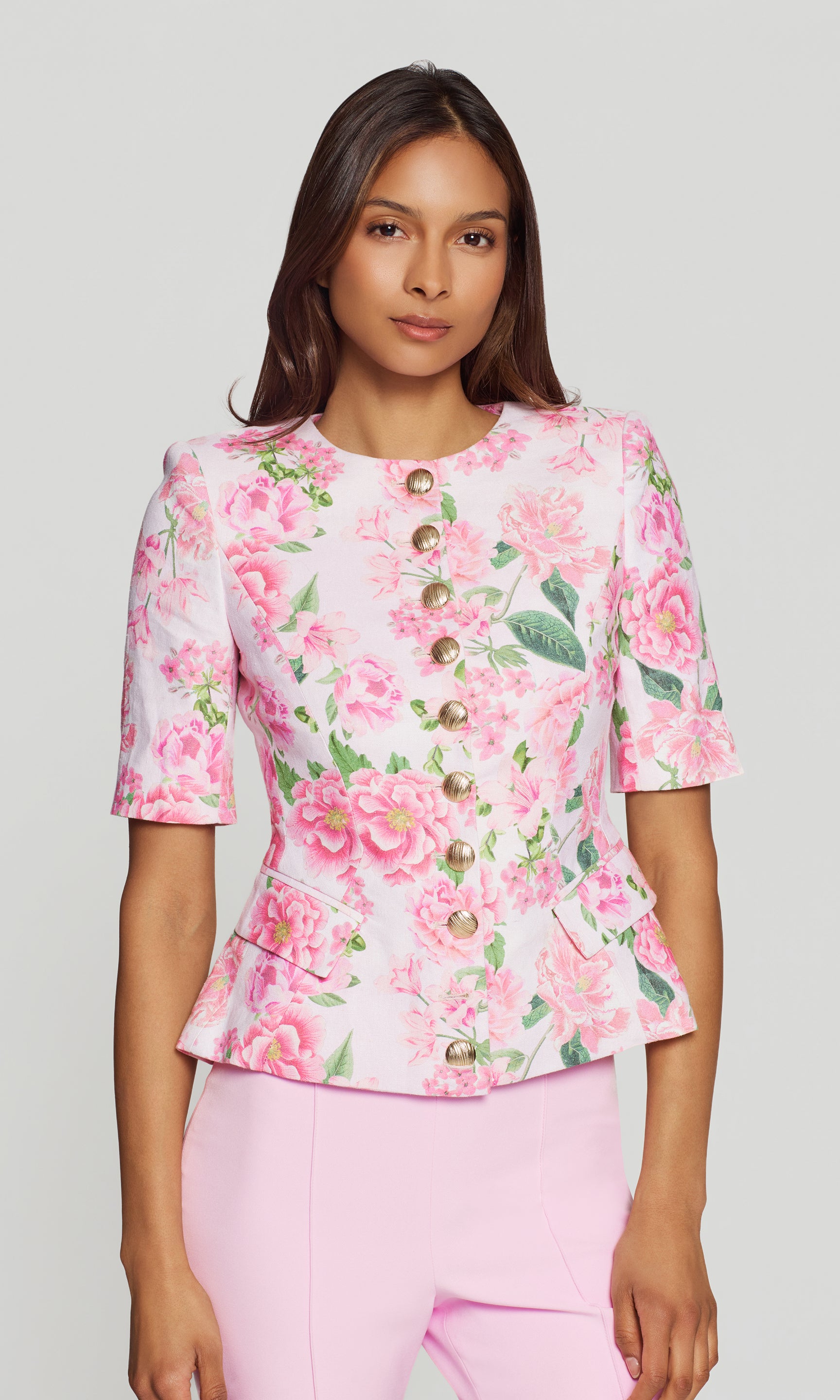 Woman wearing a pink floral jacket with gold buttons on a plain background