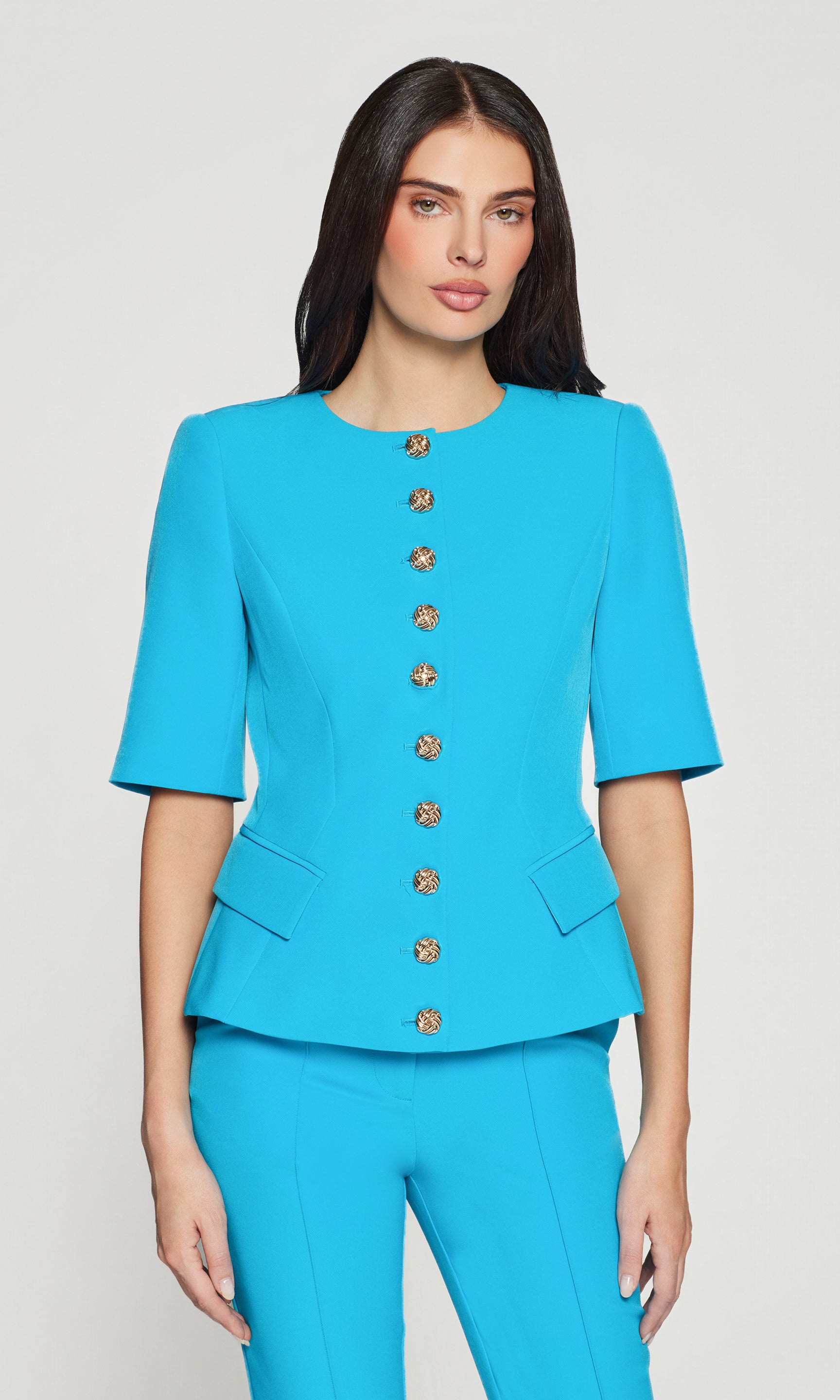 Woman wearing a turquoise suit with button details on a plain background