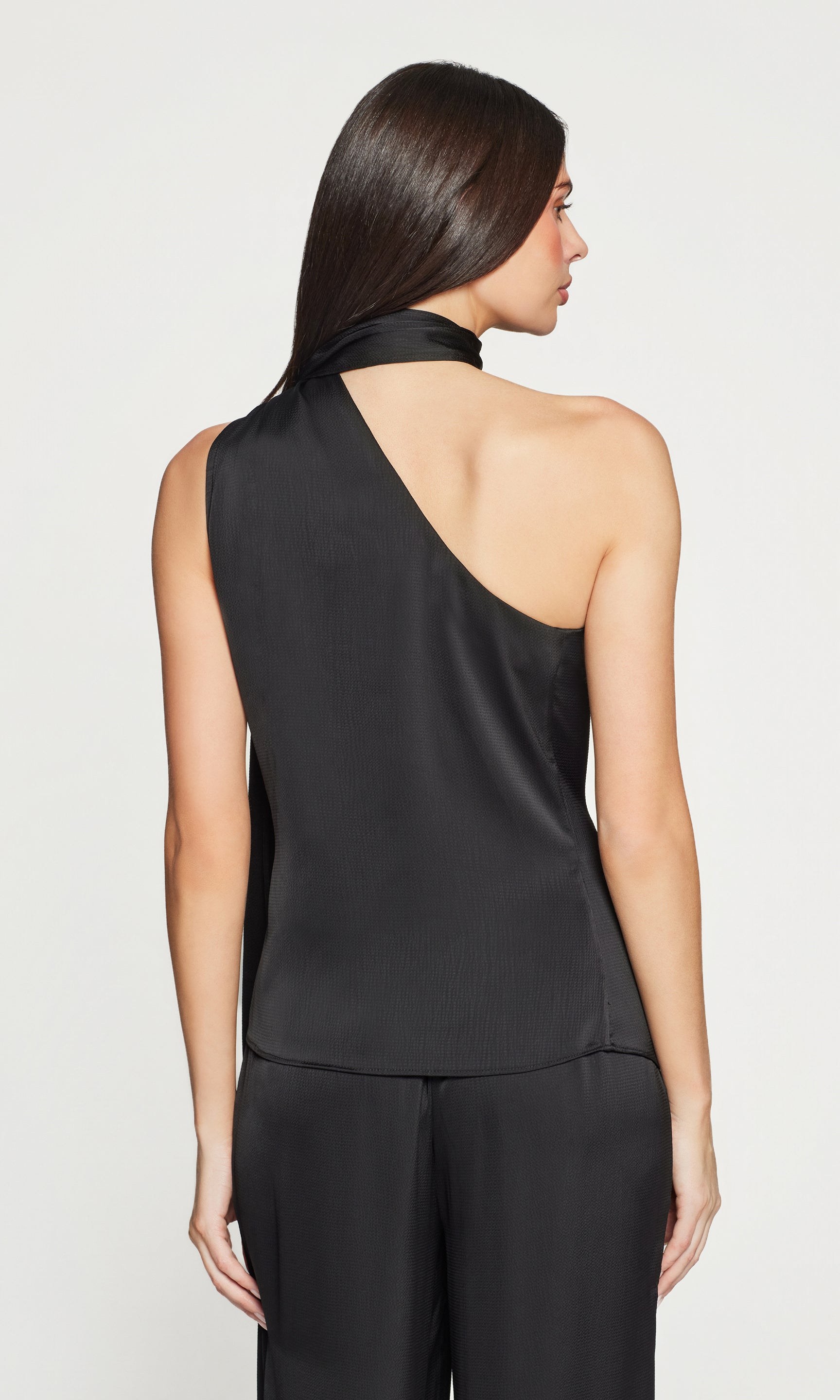 Back view of woman wearing a black one-shoulder top and black pants on a white background