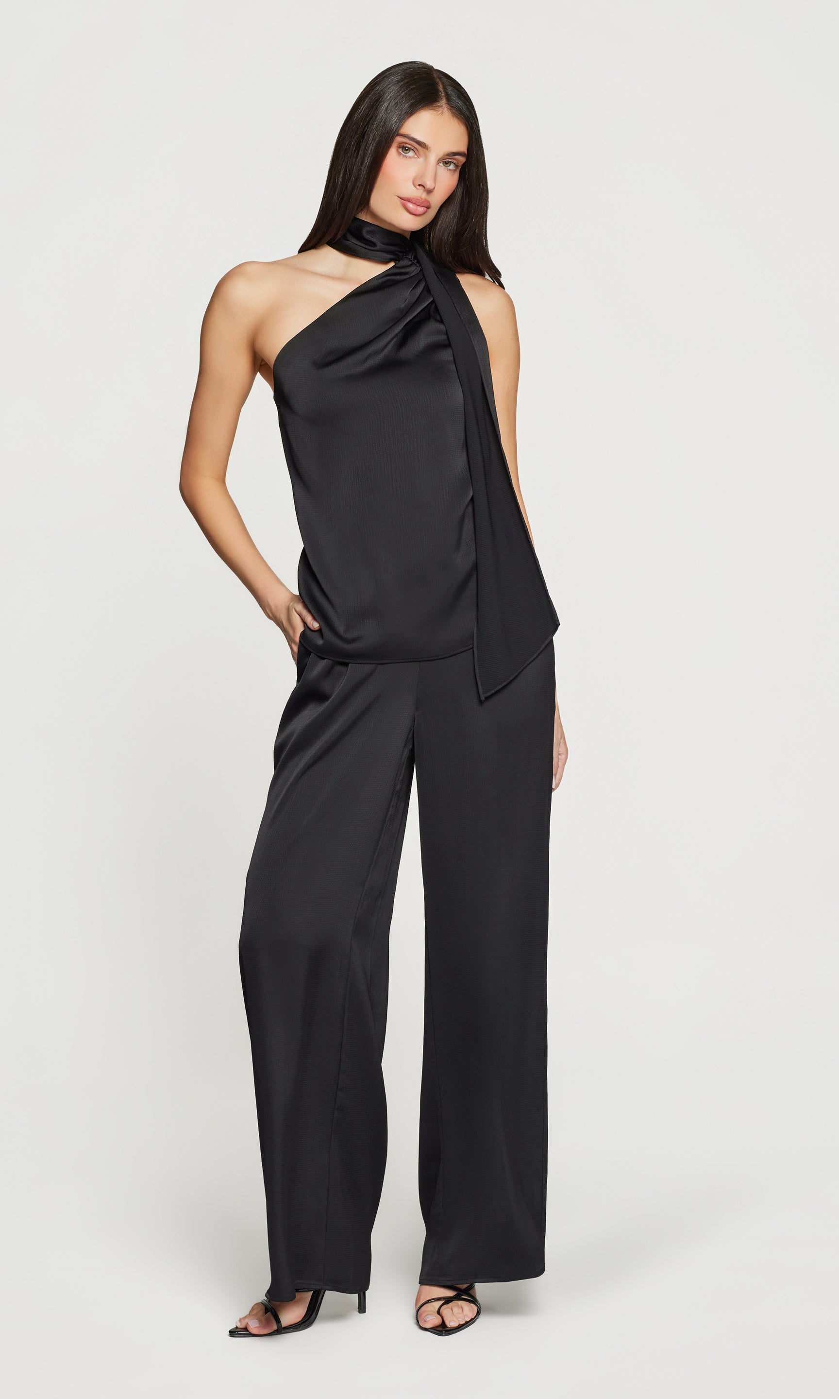 Woman wearing a black one-shoulder top and matching pants on a white background