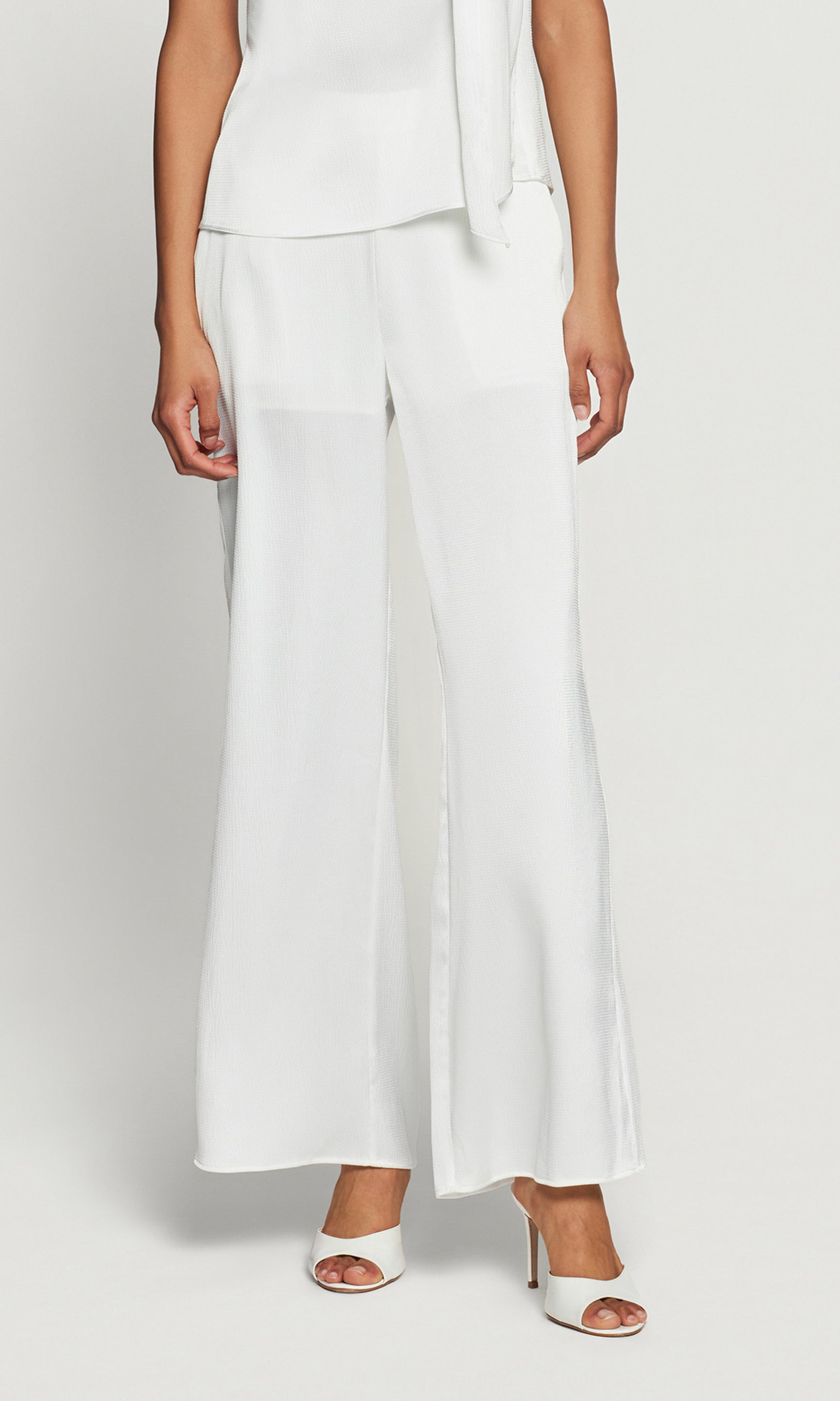 Person wearing a white outfit with wide-leg pants on a plain background