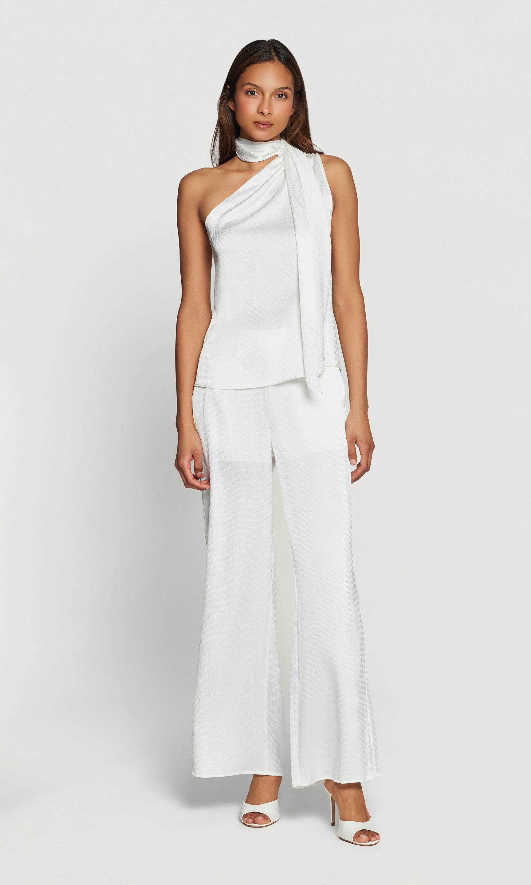 Woman wearing a white one-shoulder top and matching pant on a plain background
