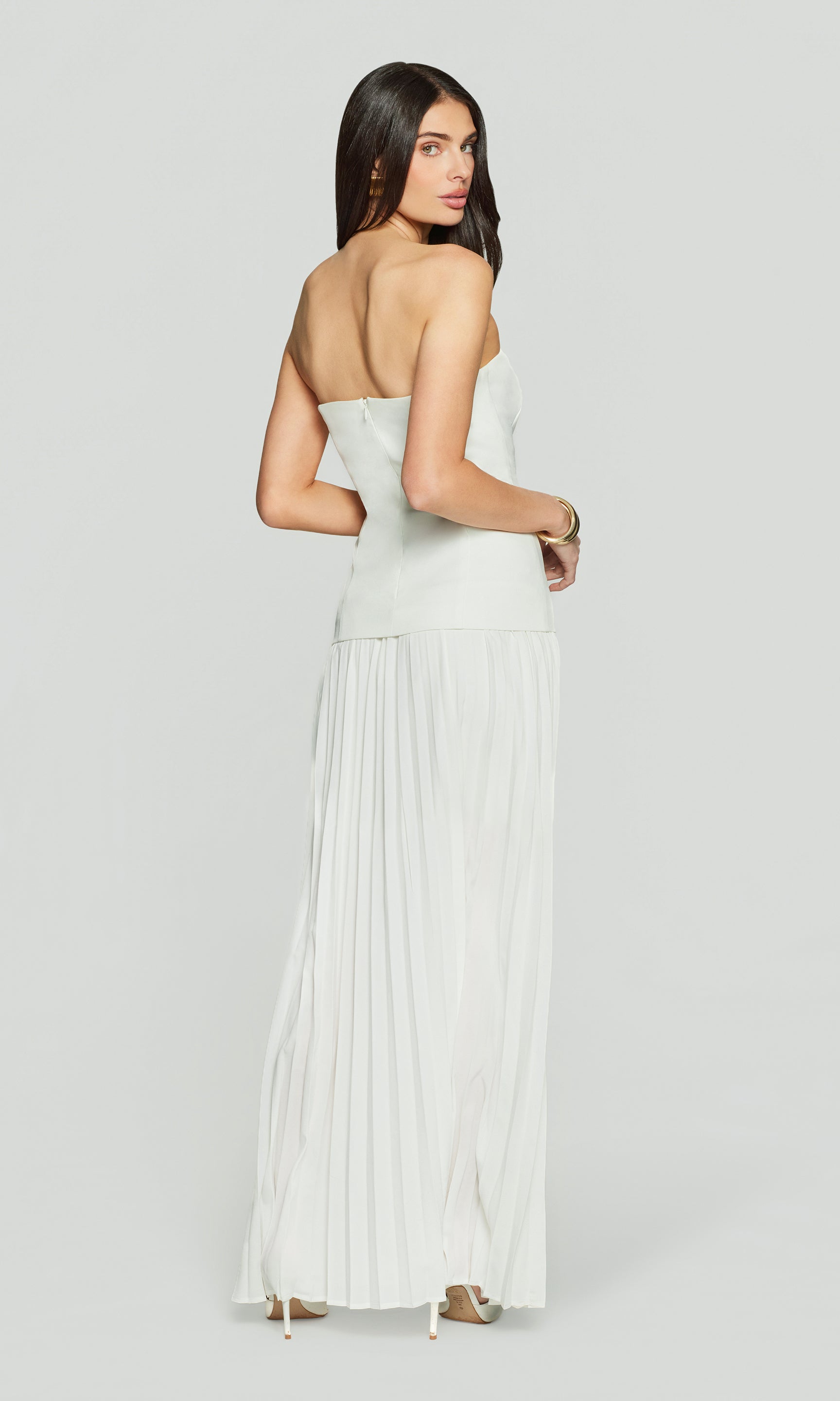Back view of woman wearing a white strapless dress on a light gray background