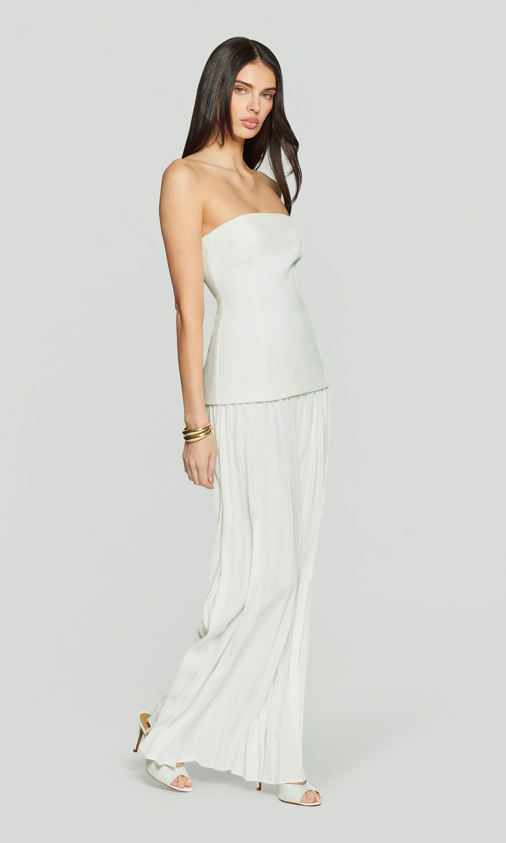 Side view of woman wearing a strapless white dress on a plain background