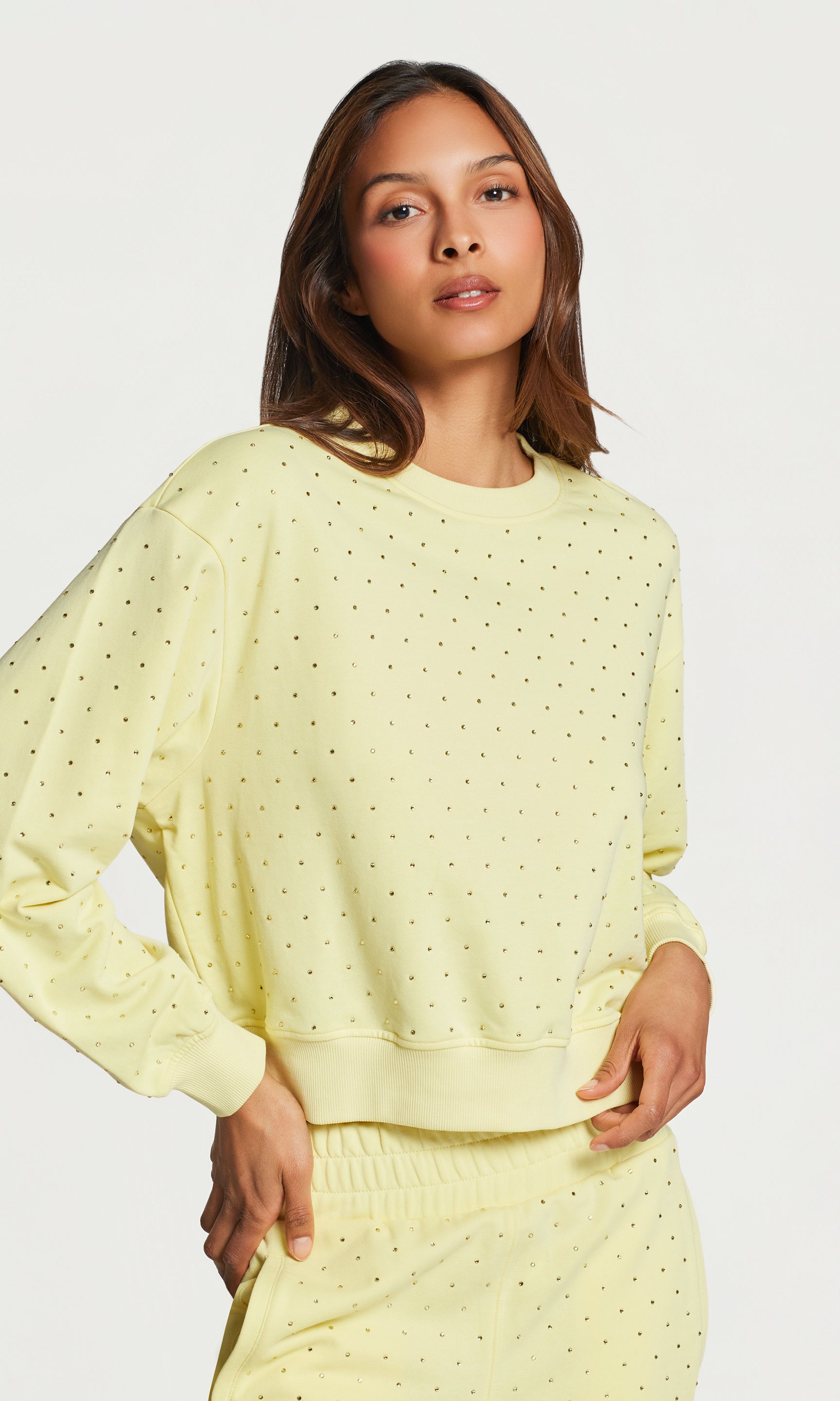 Woman wearing a light yellow polka dot sweater and pant set on a white background