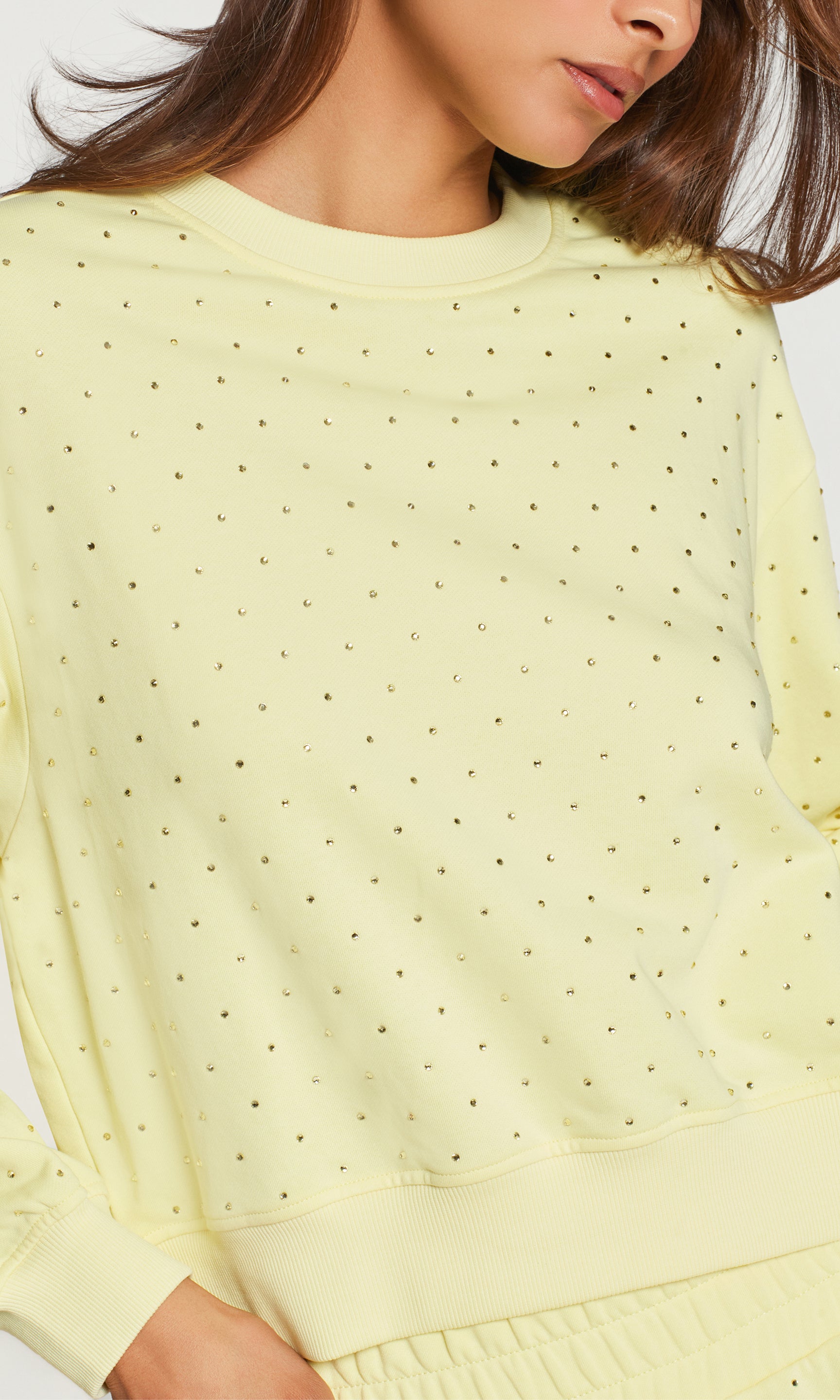 Close-up of light yellow crystal embellished sweater worn by a person on a white background