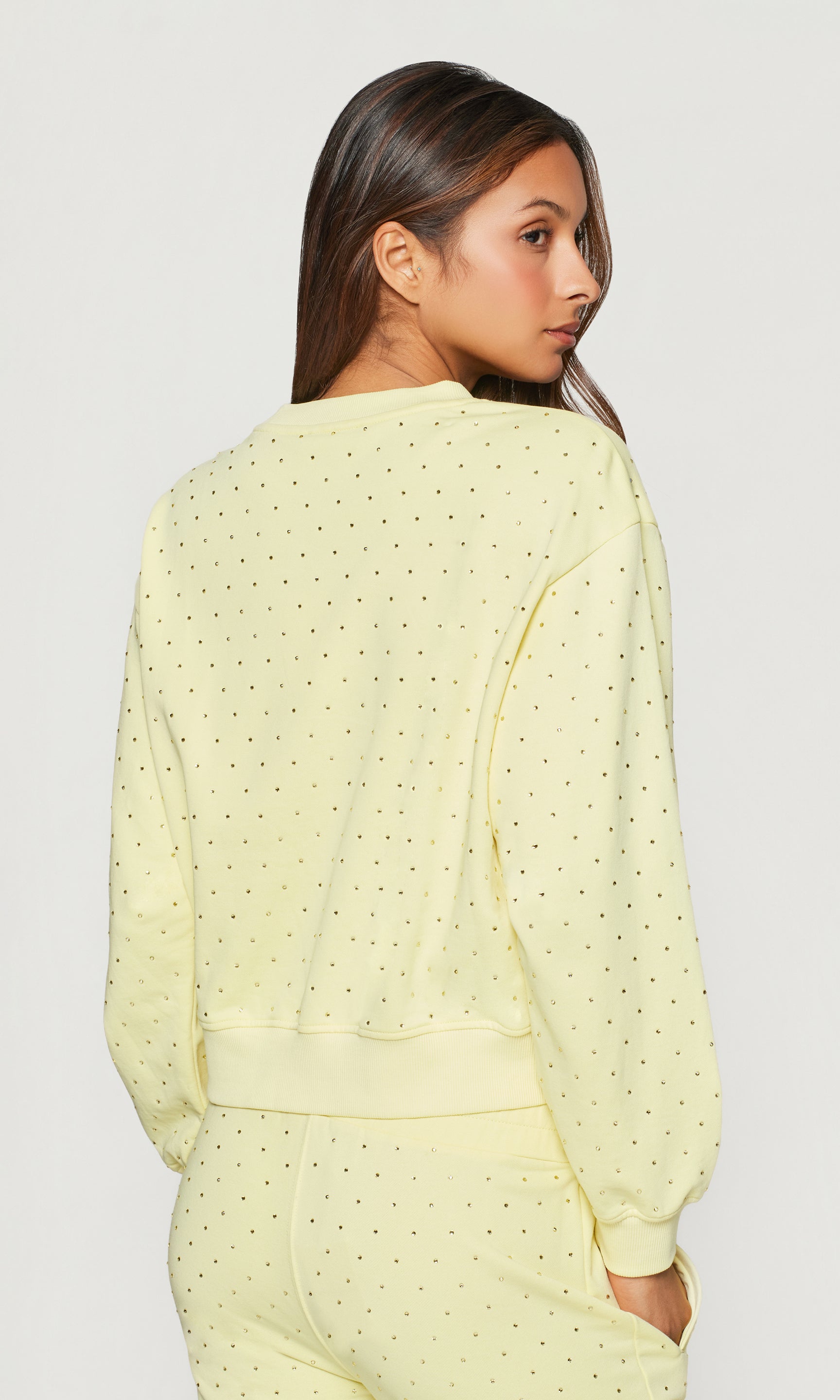 Back view of woman wearing a light yellow crystal embellished outfit on a plain background