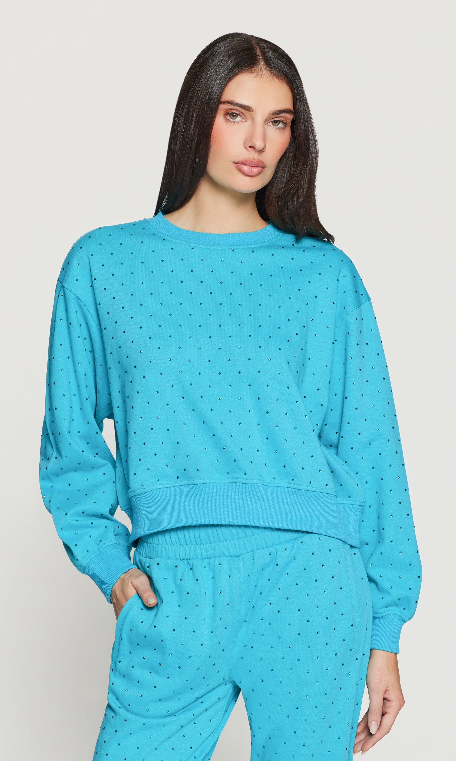 Woman wearing a blue crystal embellished sweater on a light gray background