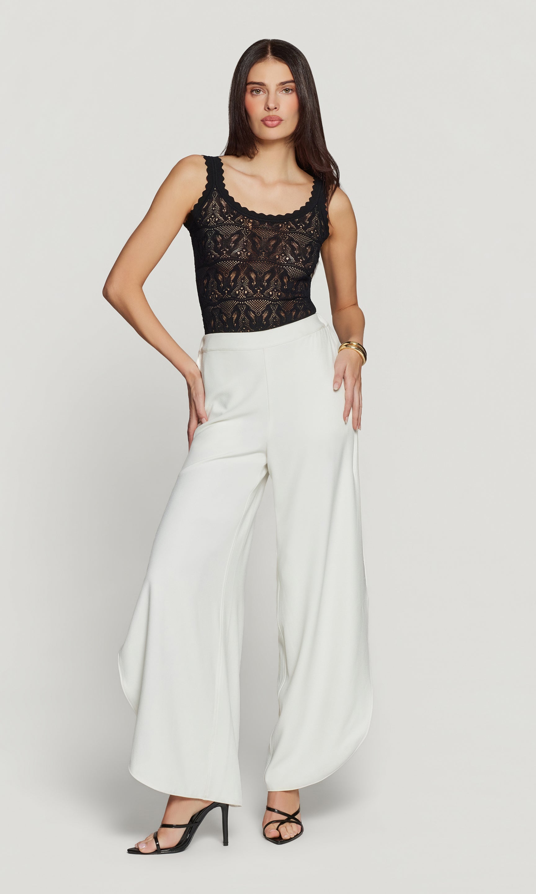Woman wearing a black lace top and white wide-leg pants on a plain background