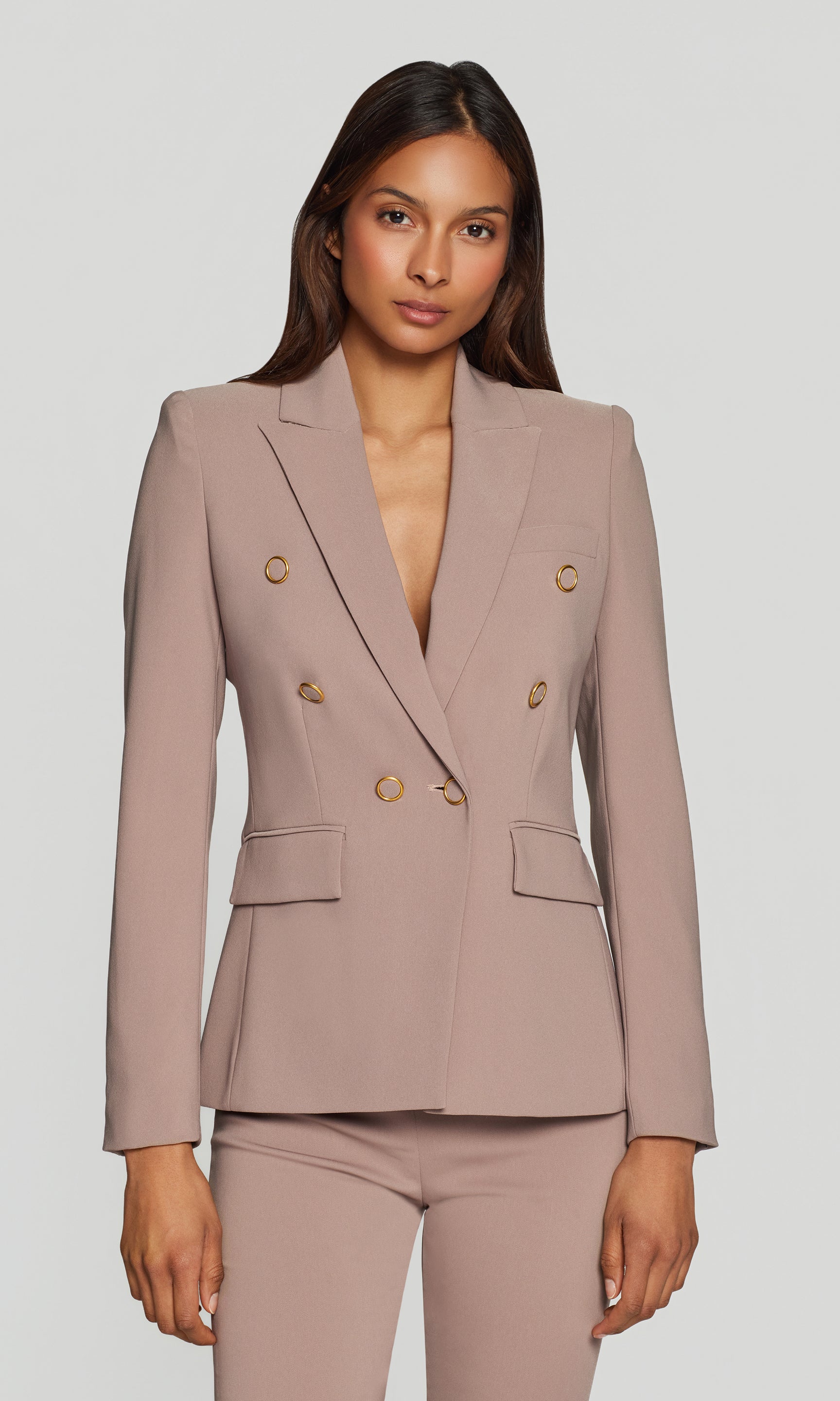 Woman wearing a beige suit with gold buttons on a plain background