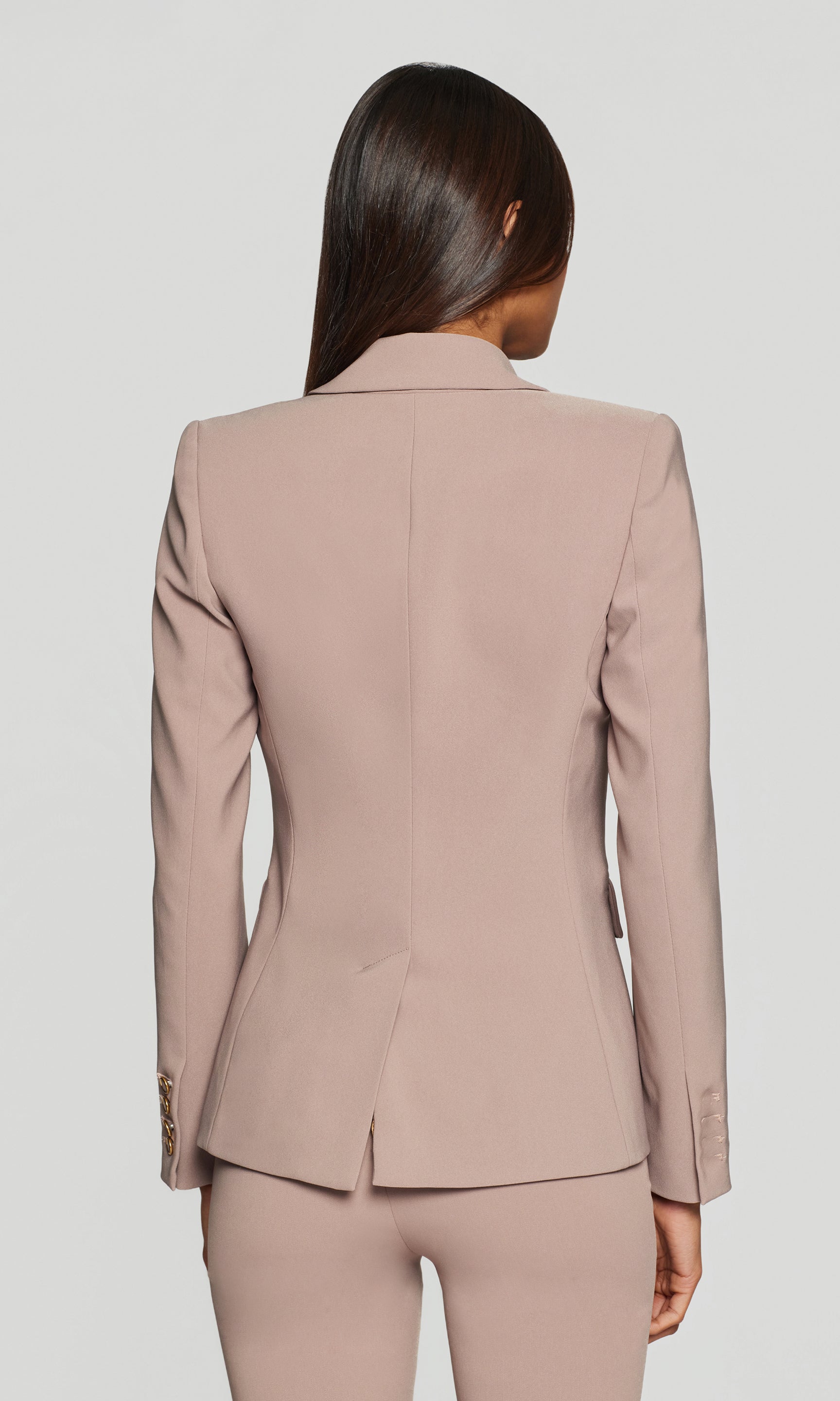 Back view of person wearing a beige suit on a plain background