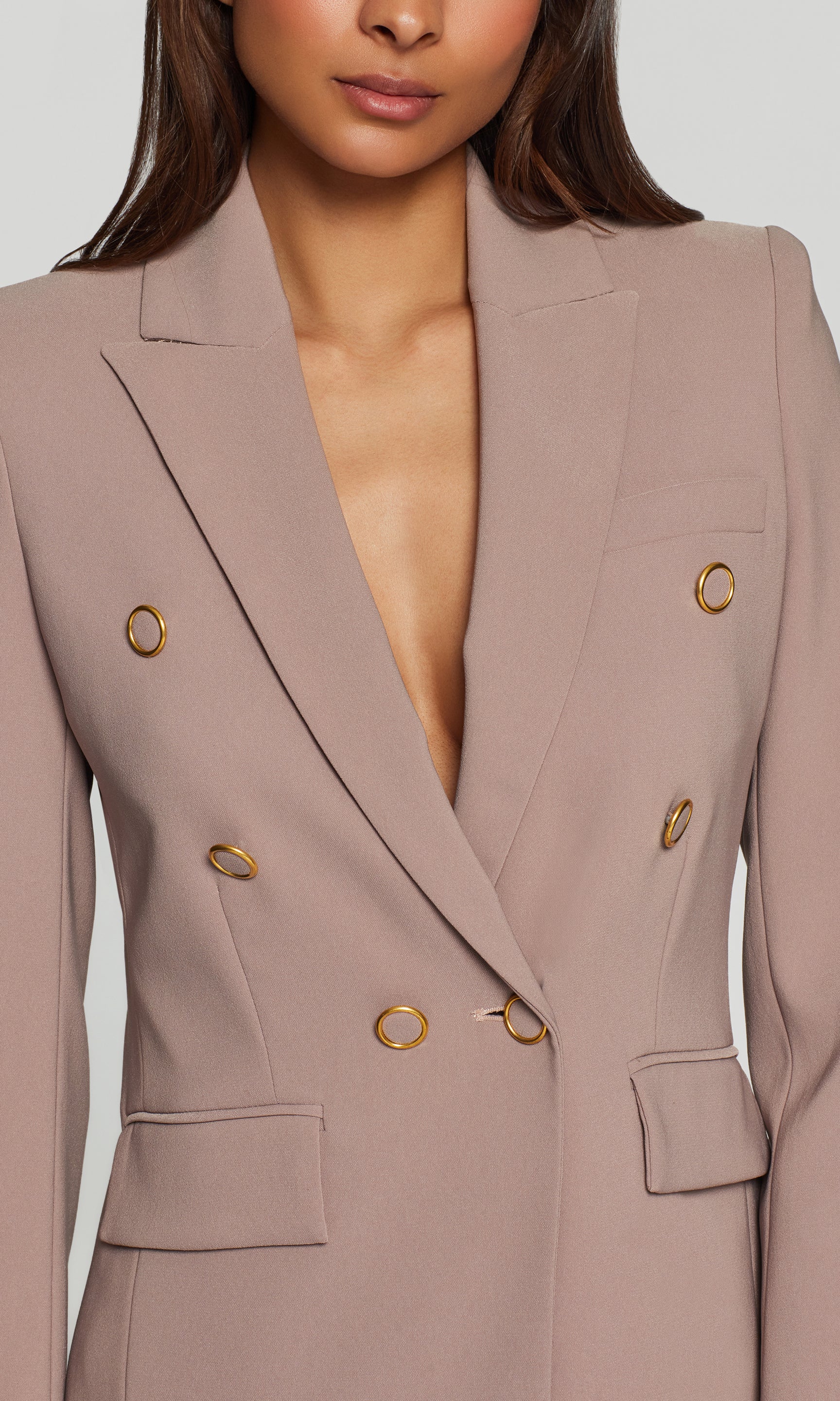 Close-up of a beige blazer with gold buttons on a plain background