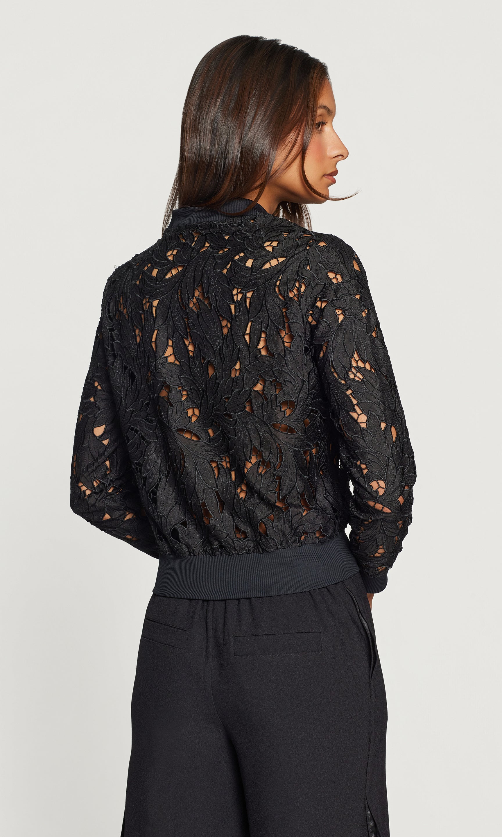 Back view of woman wearing a black lace top against a white background