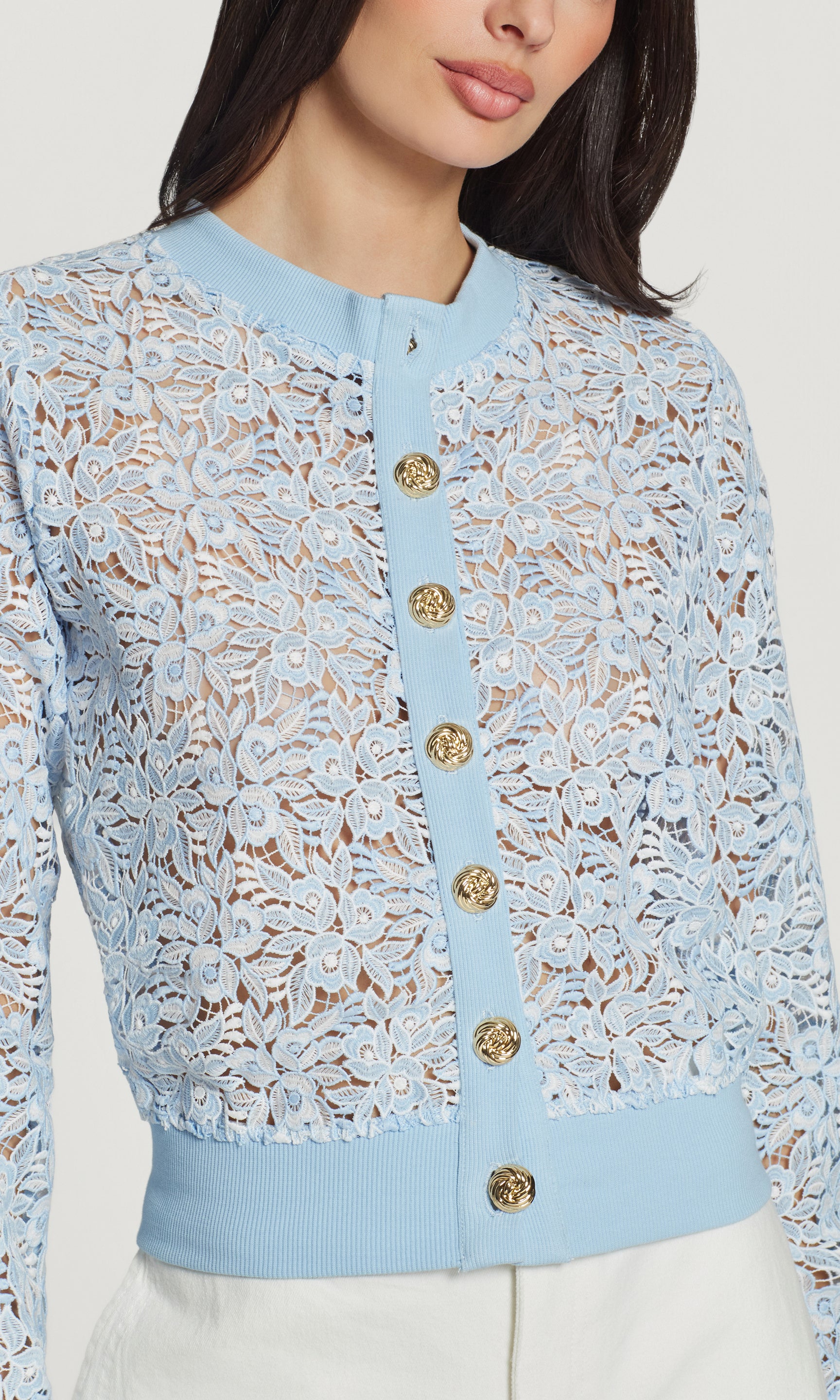 Close-up of light blue lace cardigan with gold buttons on a neutral background