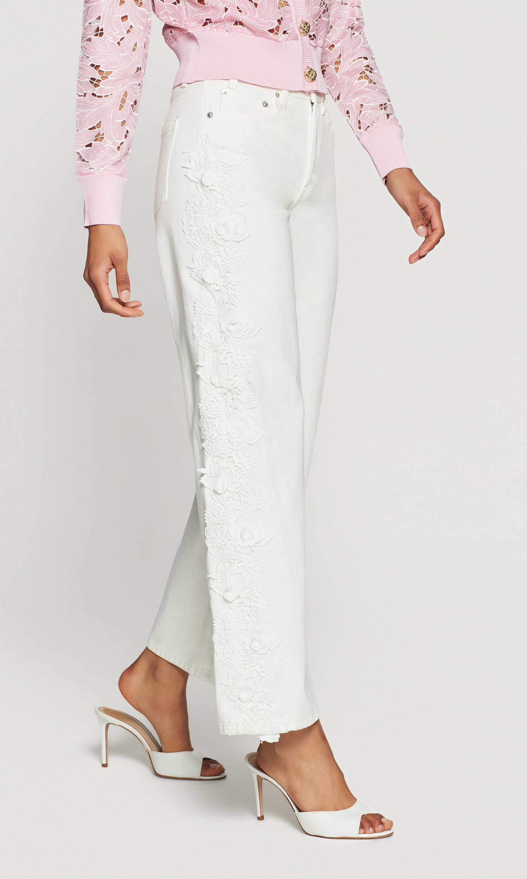 Side view of person wearing a pink floral blouse and white pants on a plain background