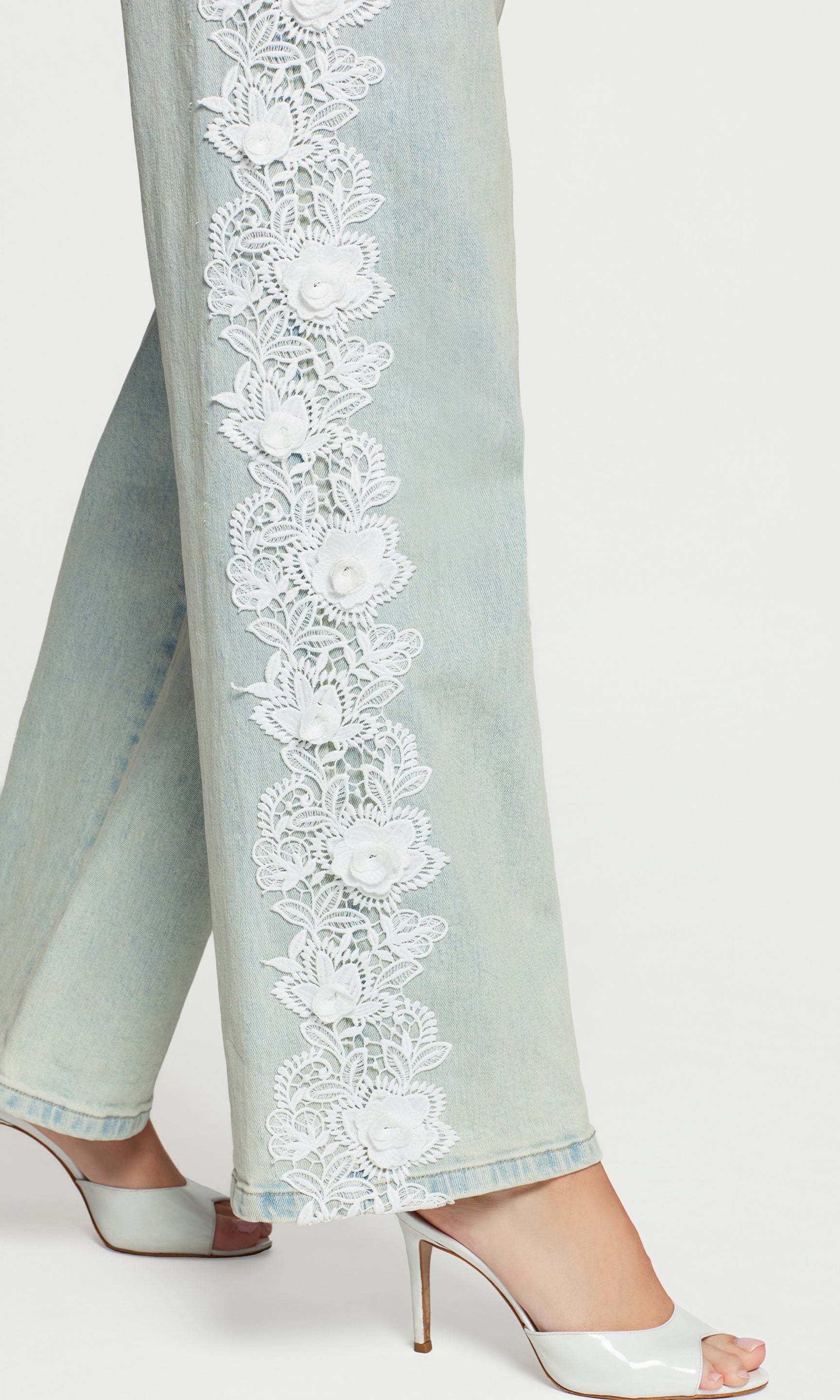 Close-up of light blue pants with white floral embroidery on a white background