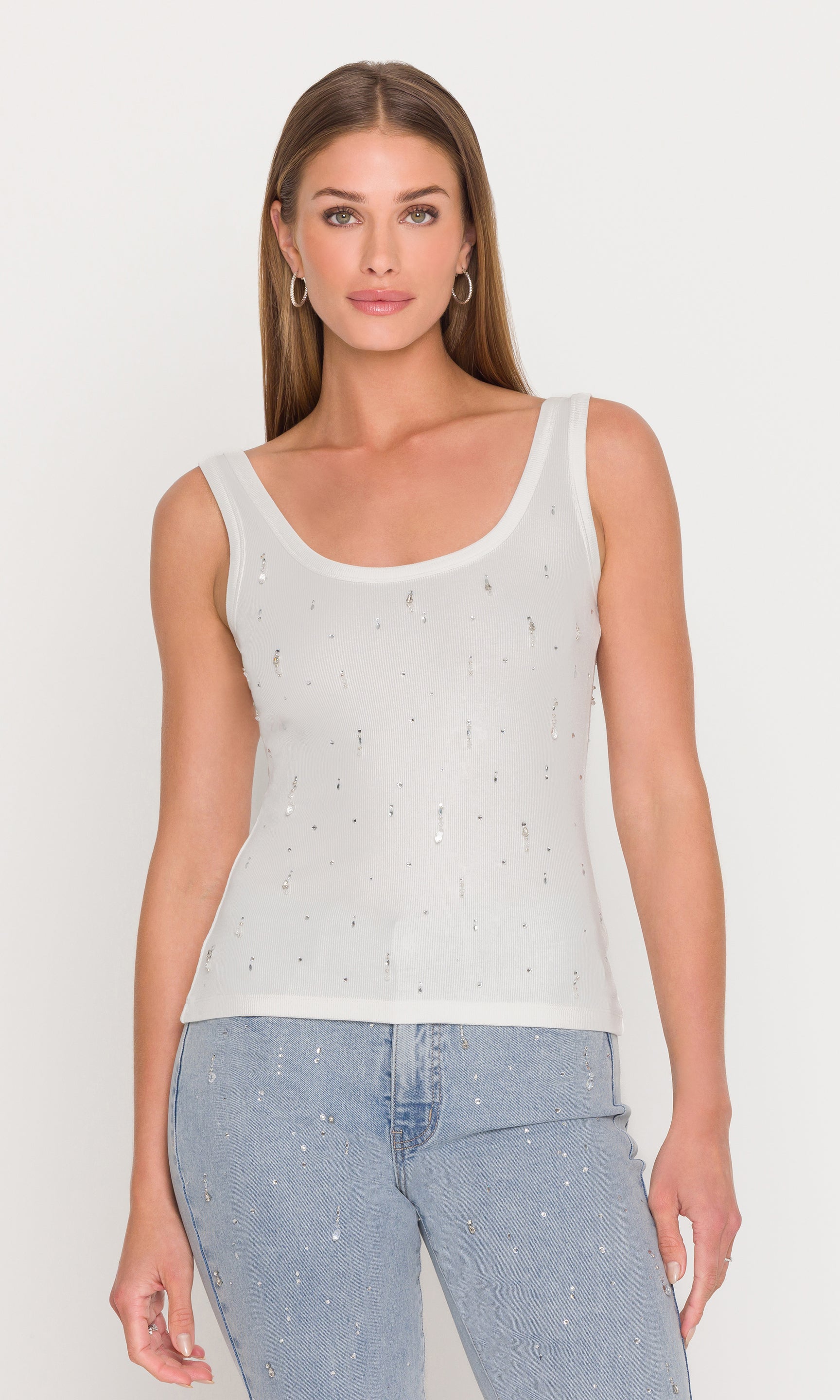 The model wears the Evita Embellished Top in white in a three-quarter front view, styled with denim to highlight the scoop neckline and allover crystal embellishments.