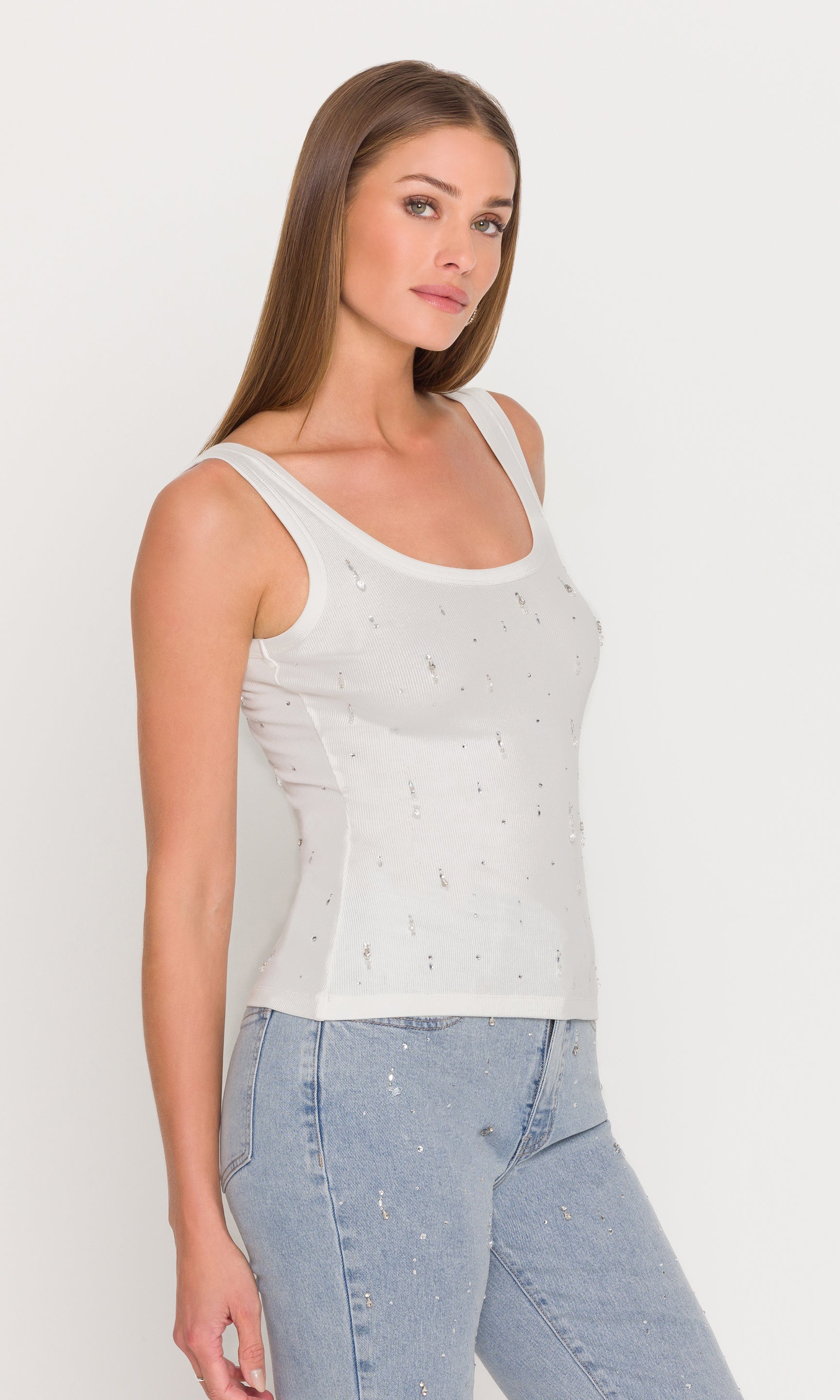 In a side view, the model wears the Evita Embellished Top in white with denim, highlighting the flattering profile and subtle crystal shine.