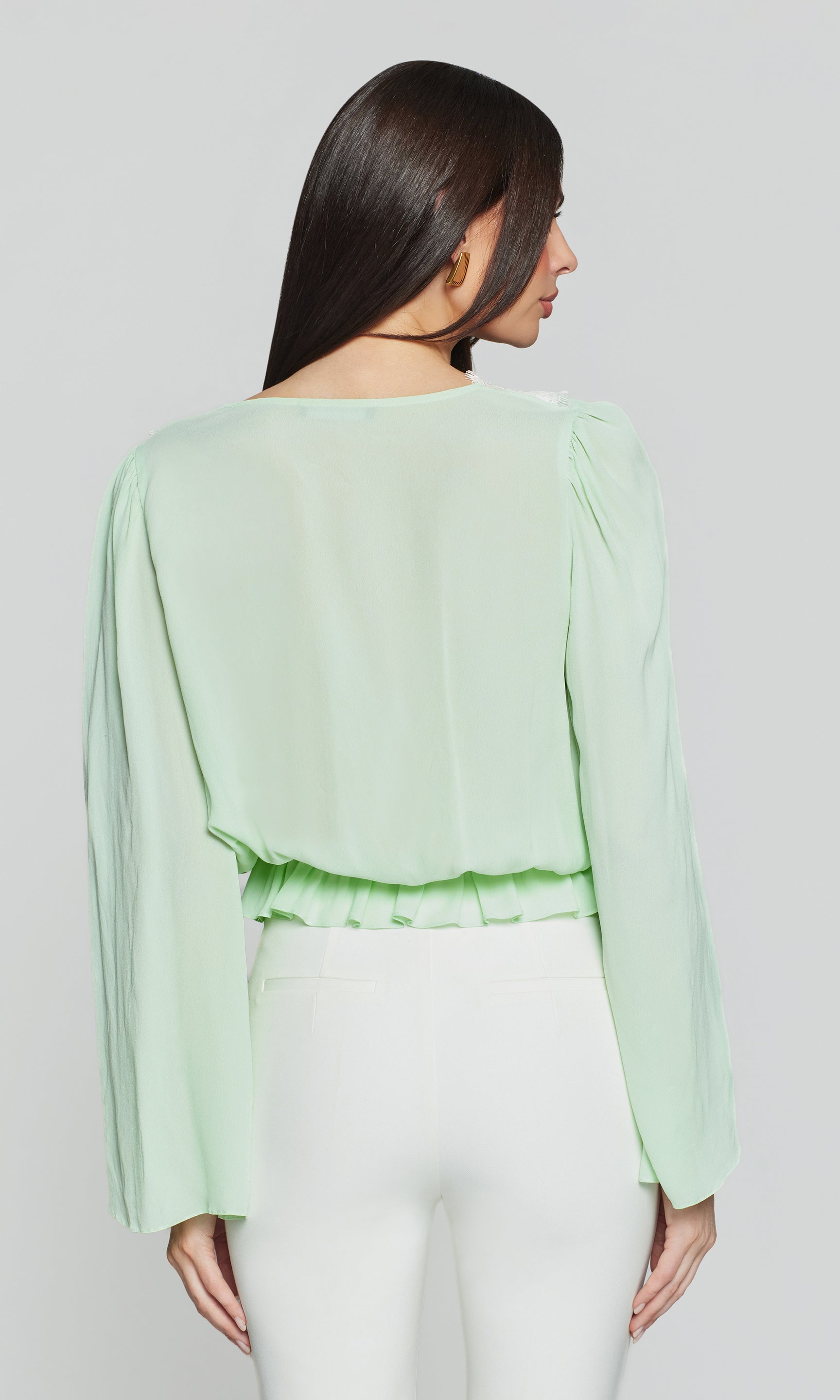 Back view of woman wearing a light green blouse with long sleeves on a plain background