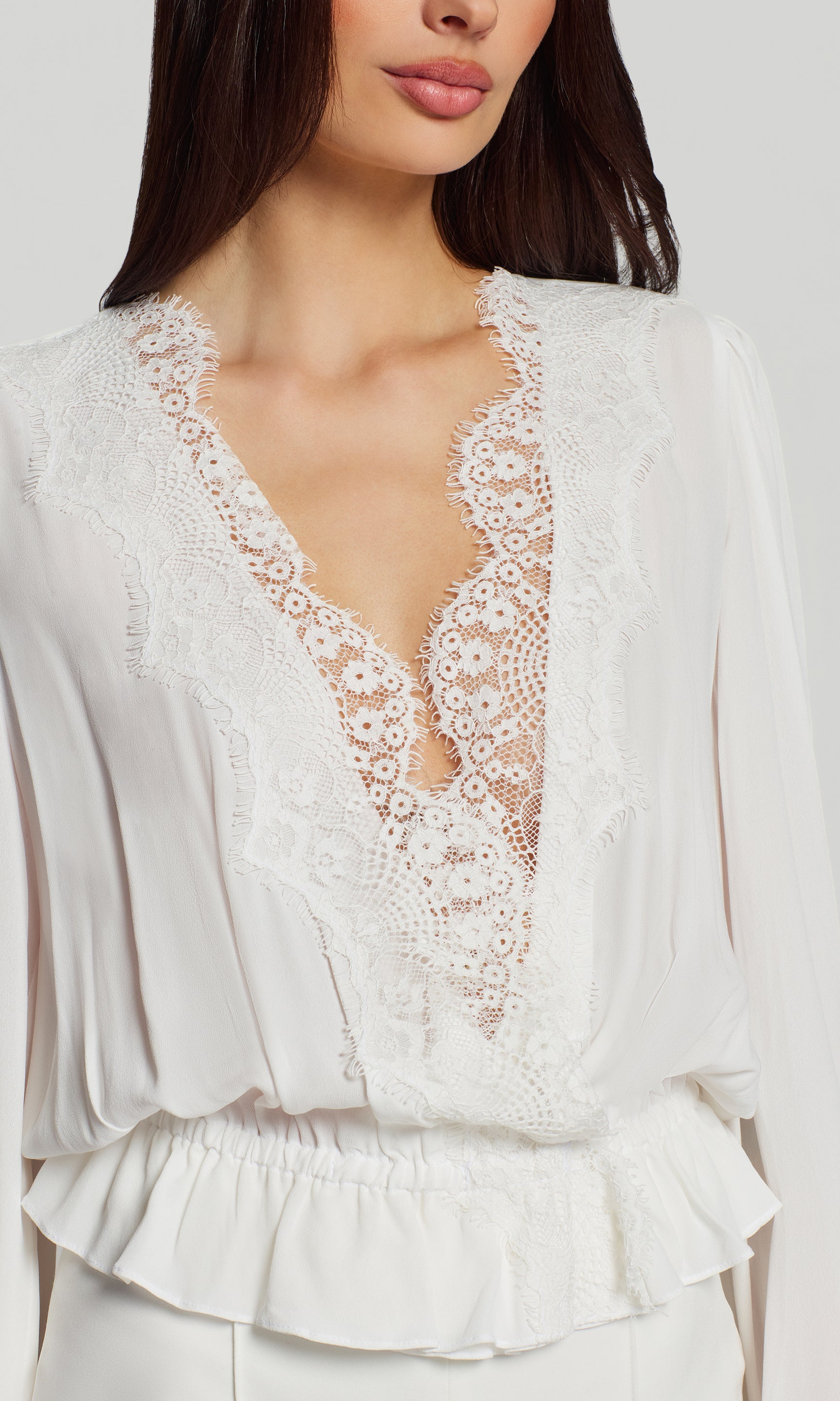White lace top with a plunging neckline on a plain background