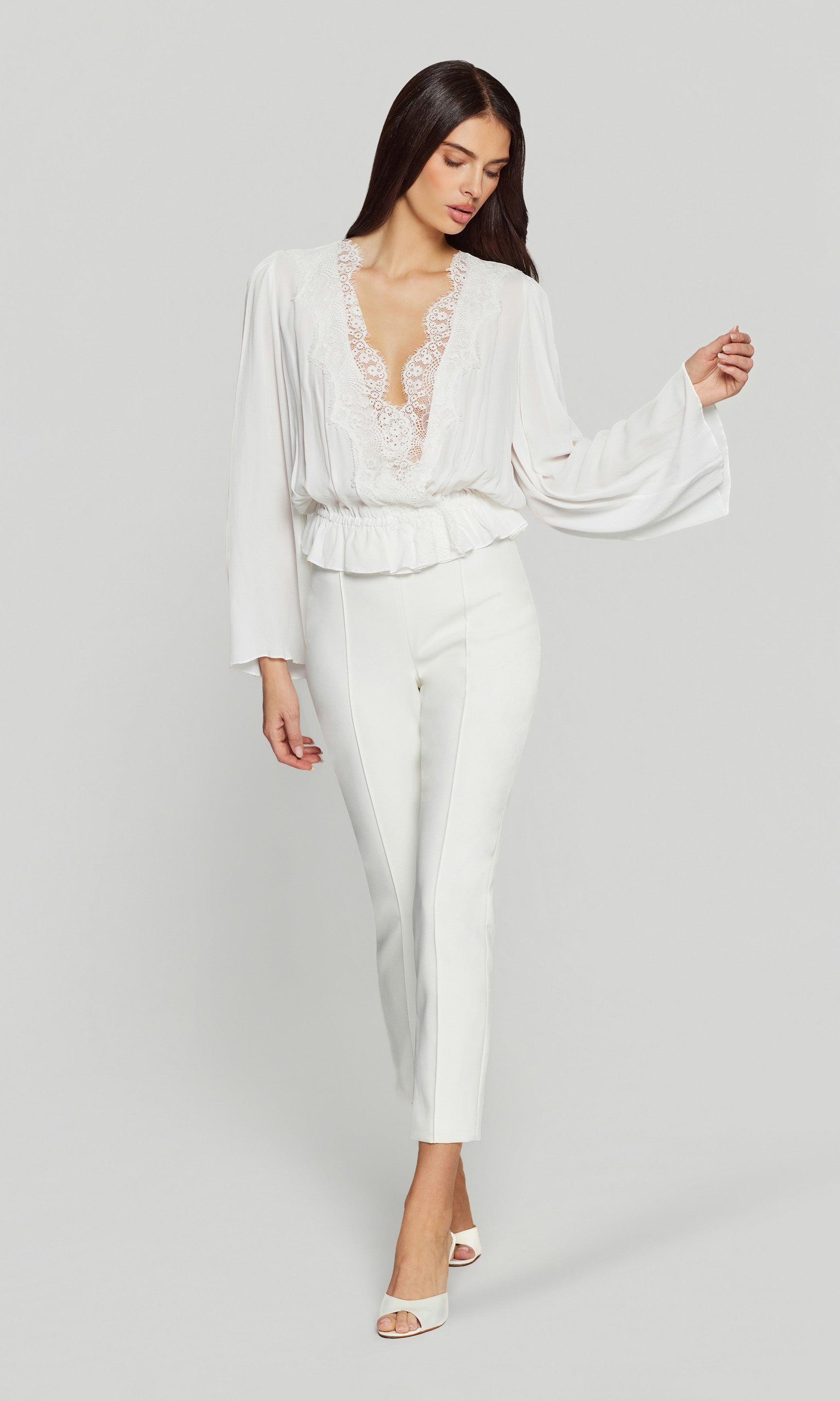 Woman wearing a white outfit with a sheer overlay on a plain background
