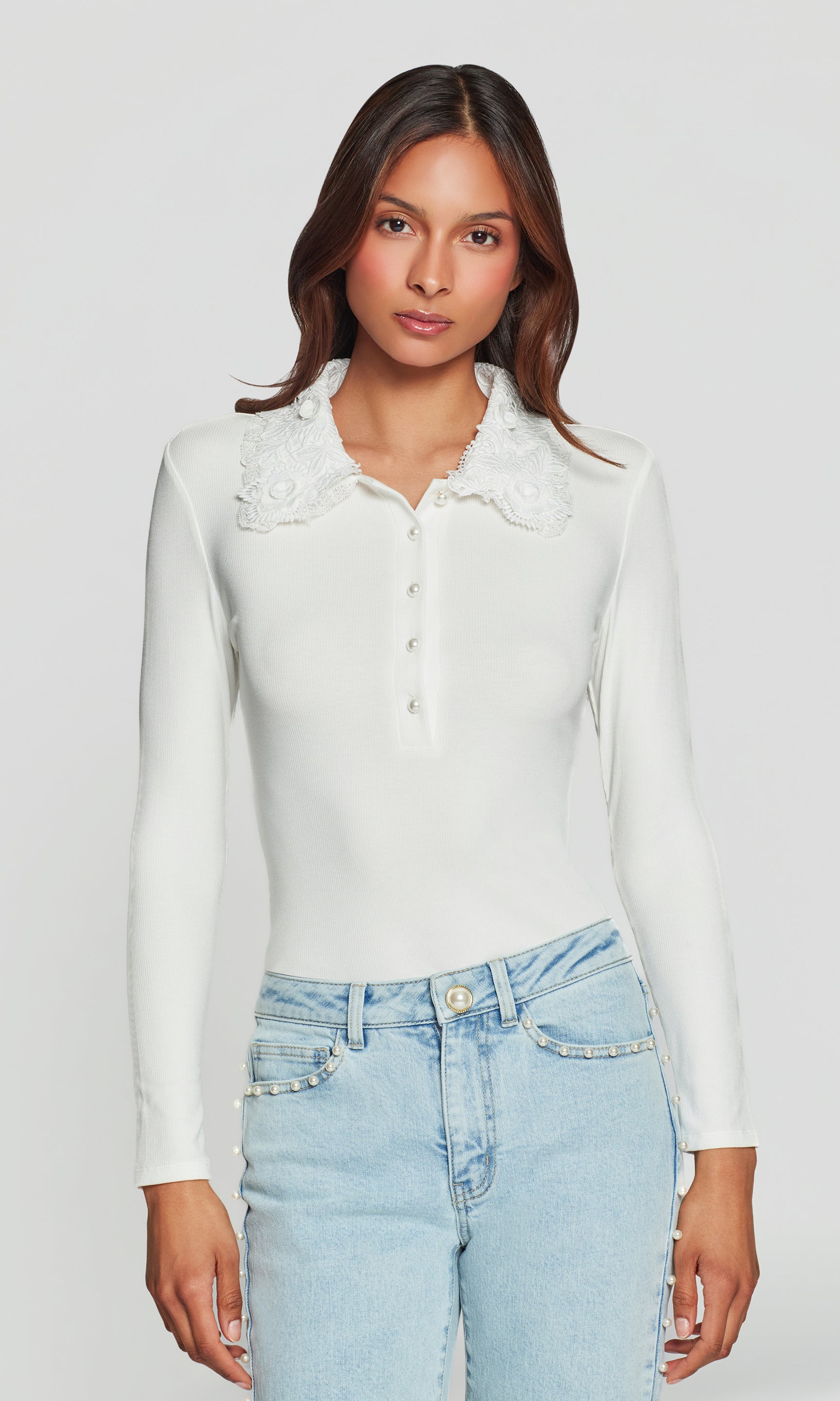 Woman wearing a white blouse with lace collar and light blue jeans on a plain background
