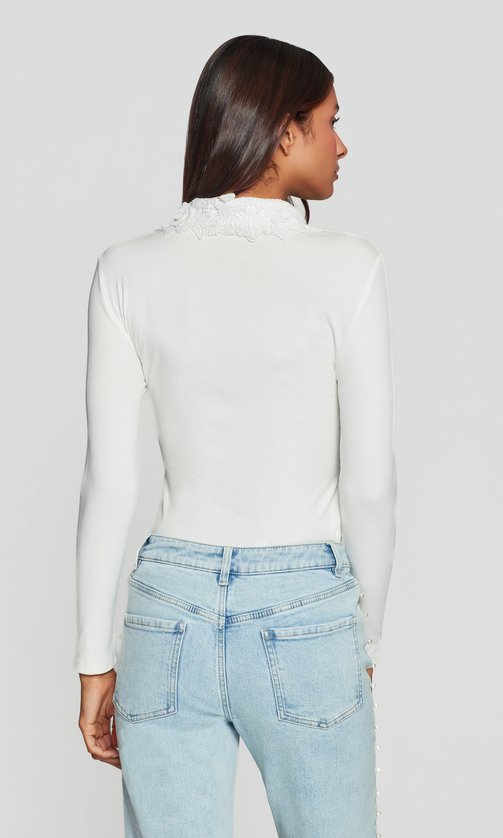 Back view of person wearing a white long-sleeve top and light blue jeans on a plain background