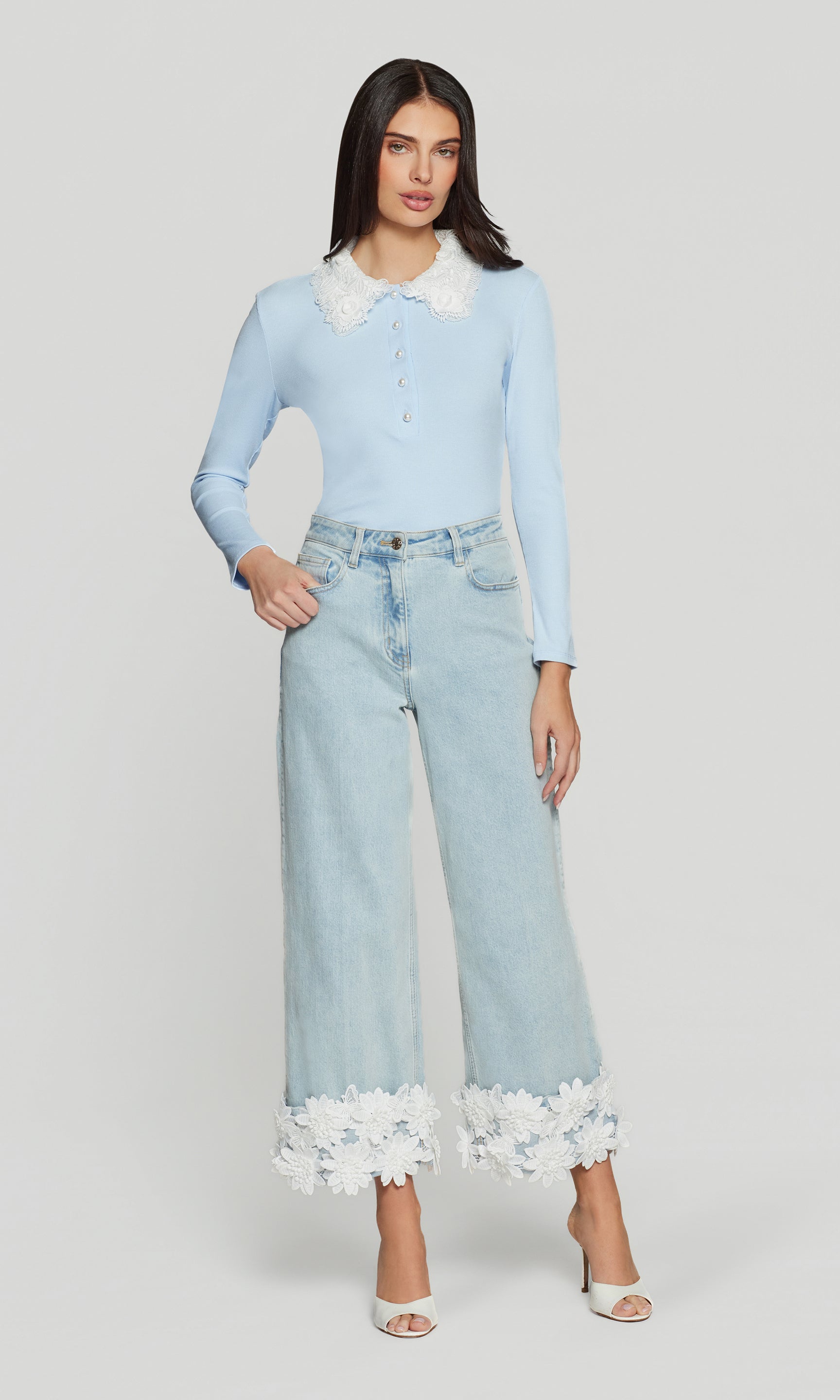 Woman wearing a light blue top and jeans with white lace trim on a white background