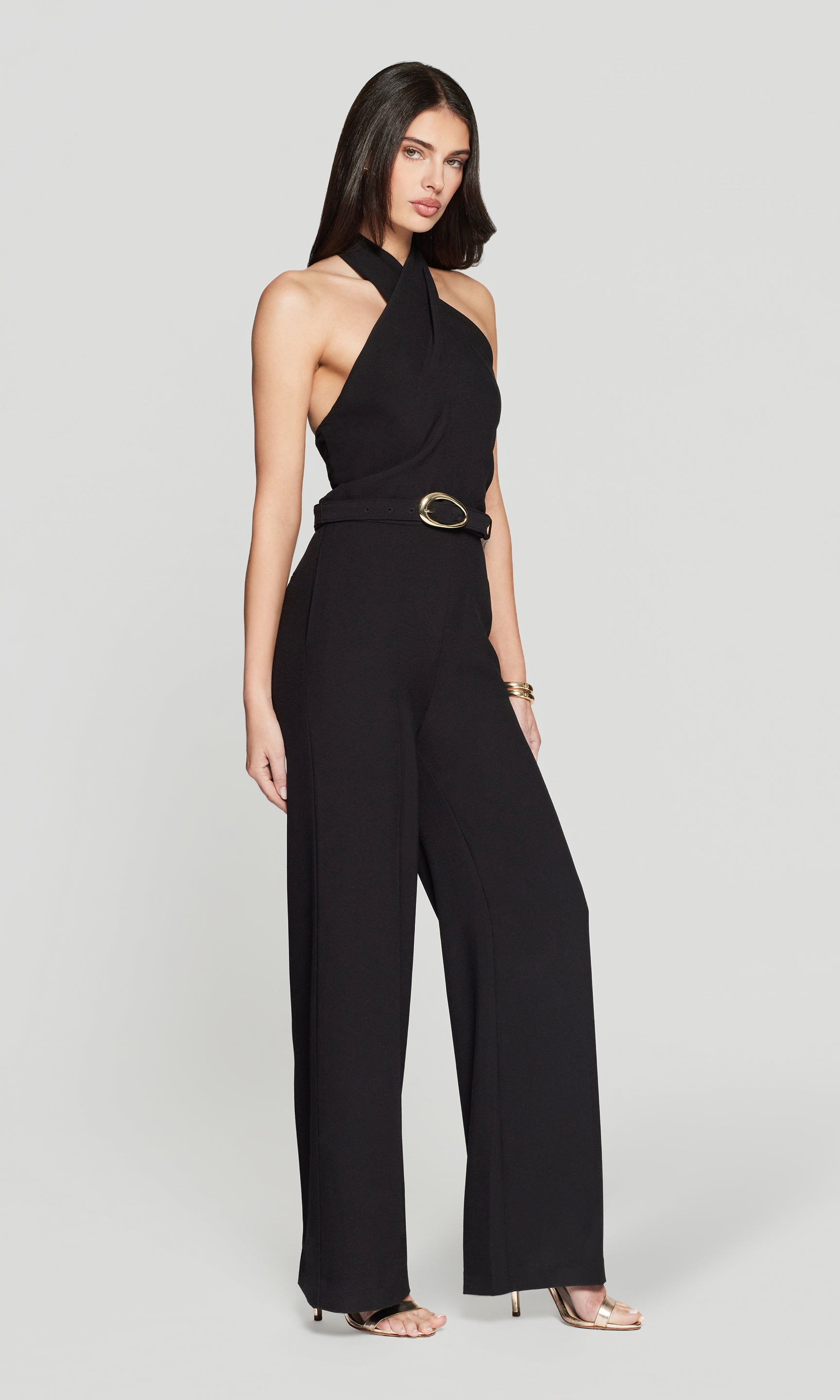 Woman wearing a black halter neck jumpsuit with a belt on a light gray background