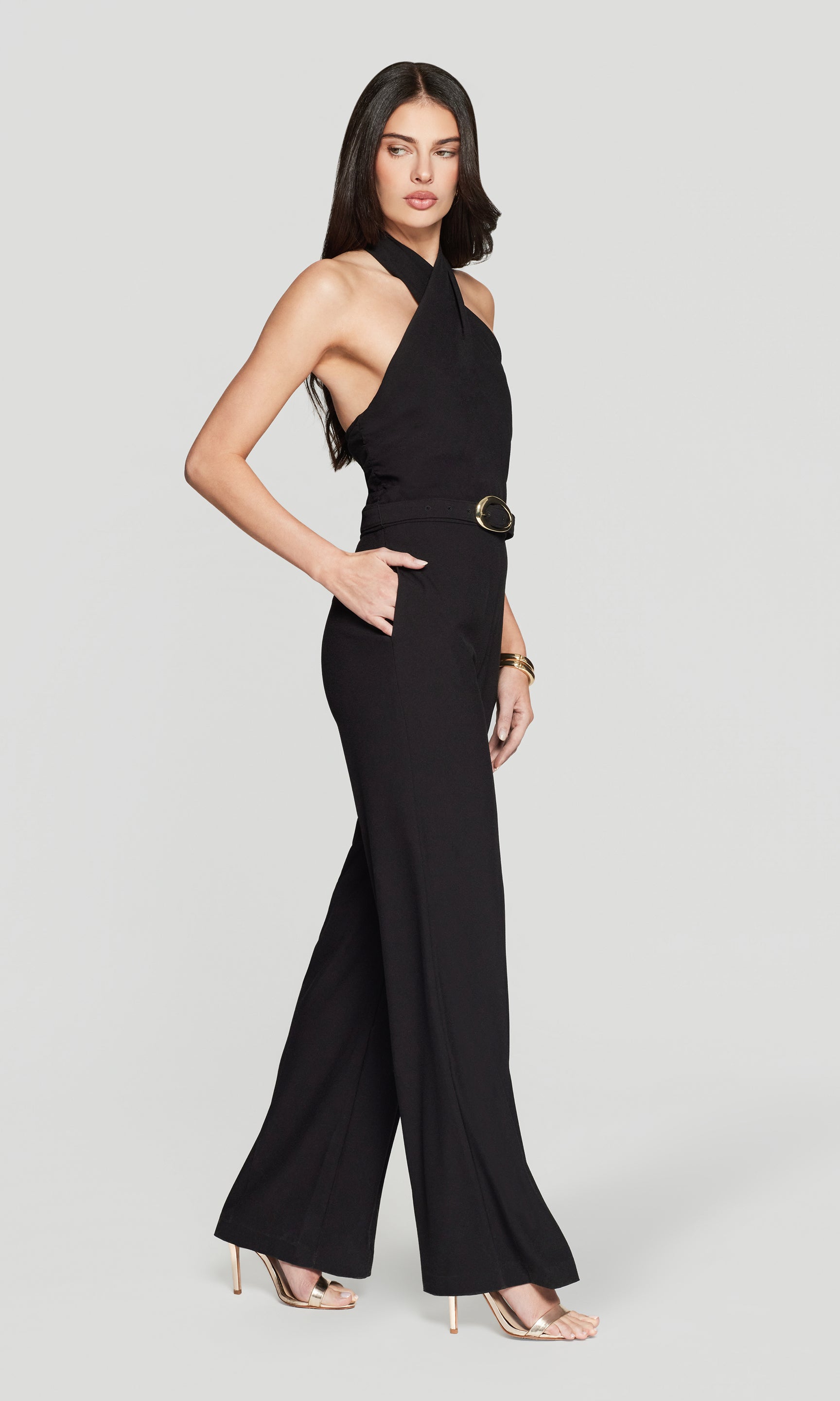 Side view of woman wearing a black jumpsuit on a light gray background