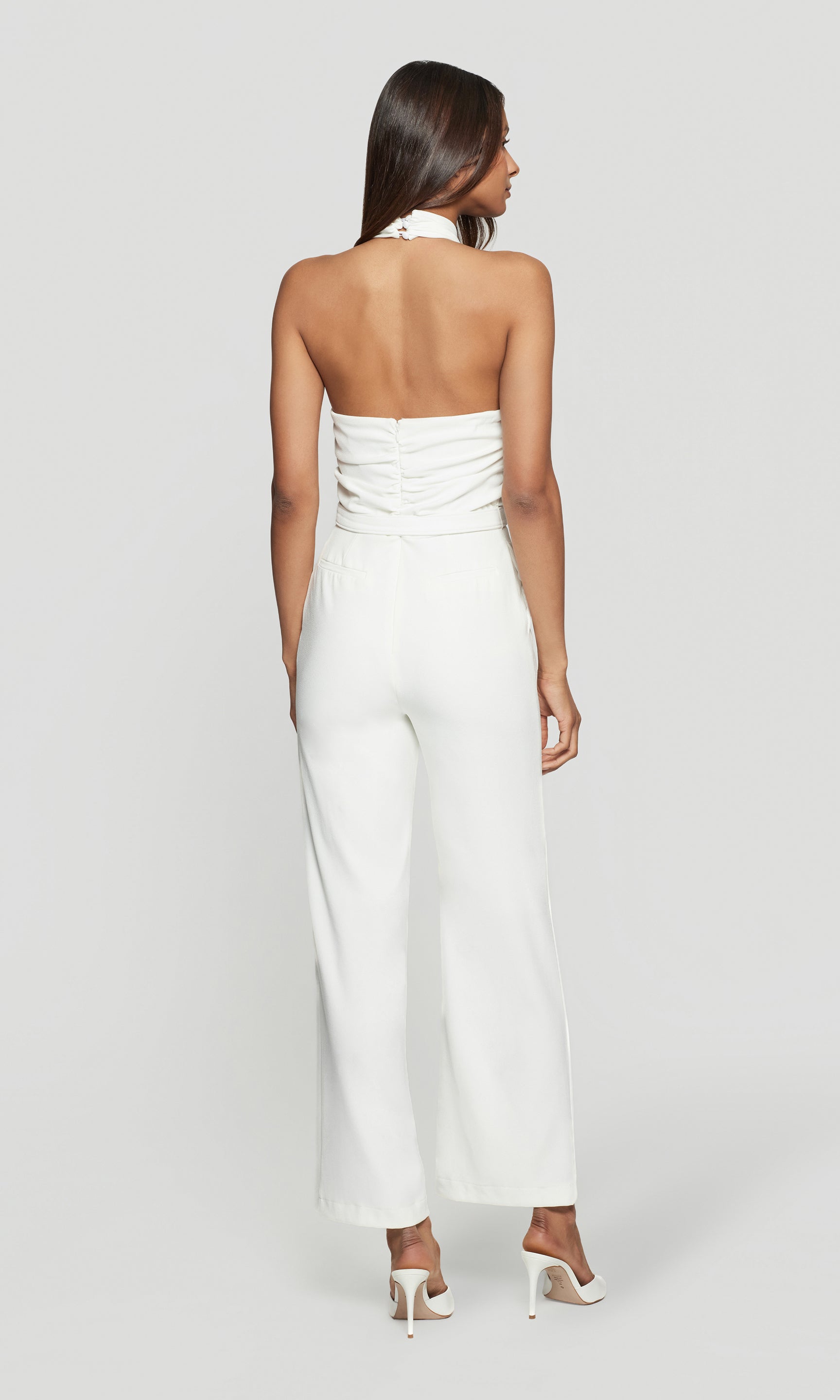 Back view of woman wearing a white strapless jumpsuit on a plain background