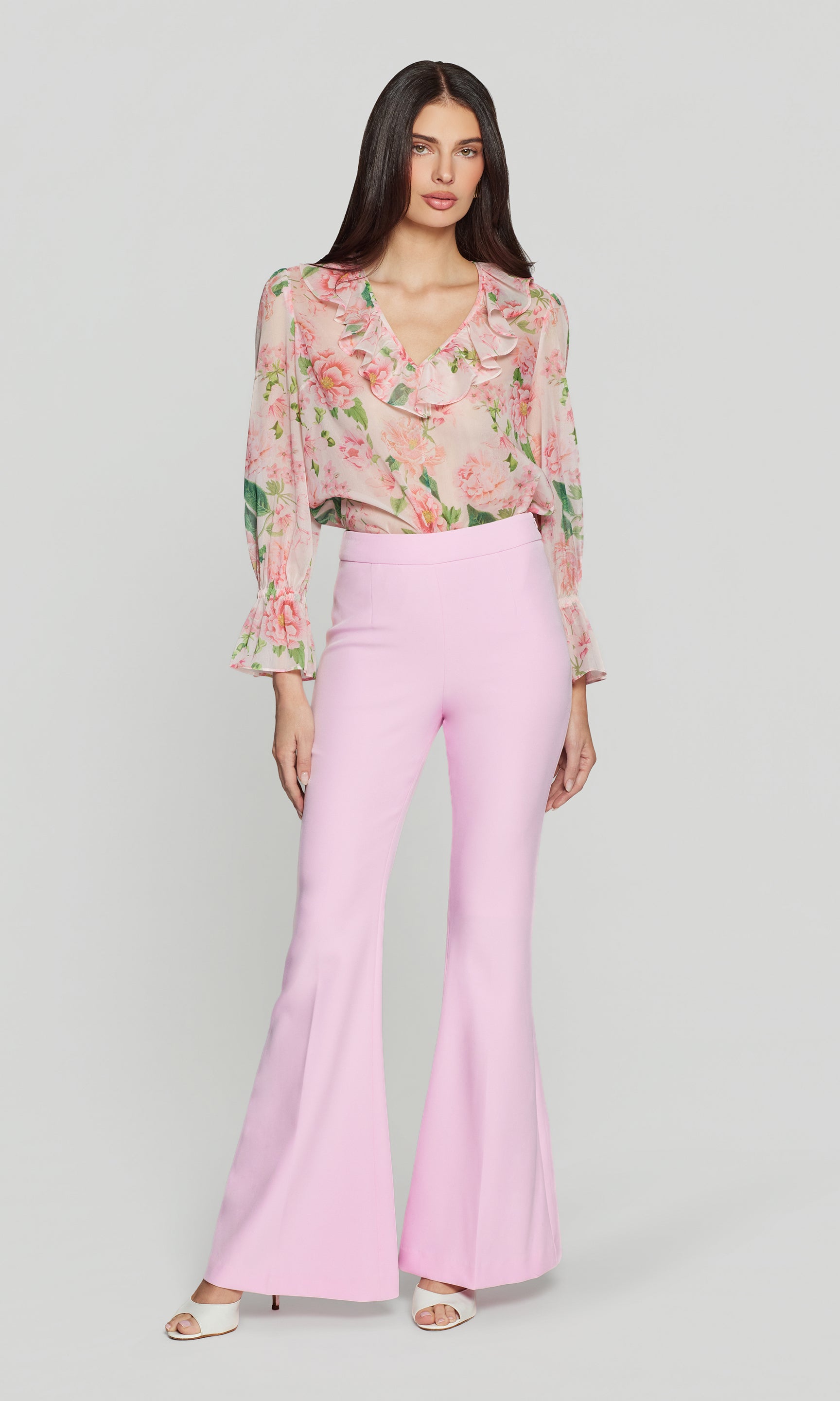 Woman wearing a floral blouse and pink pants on a gray background