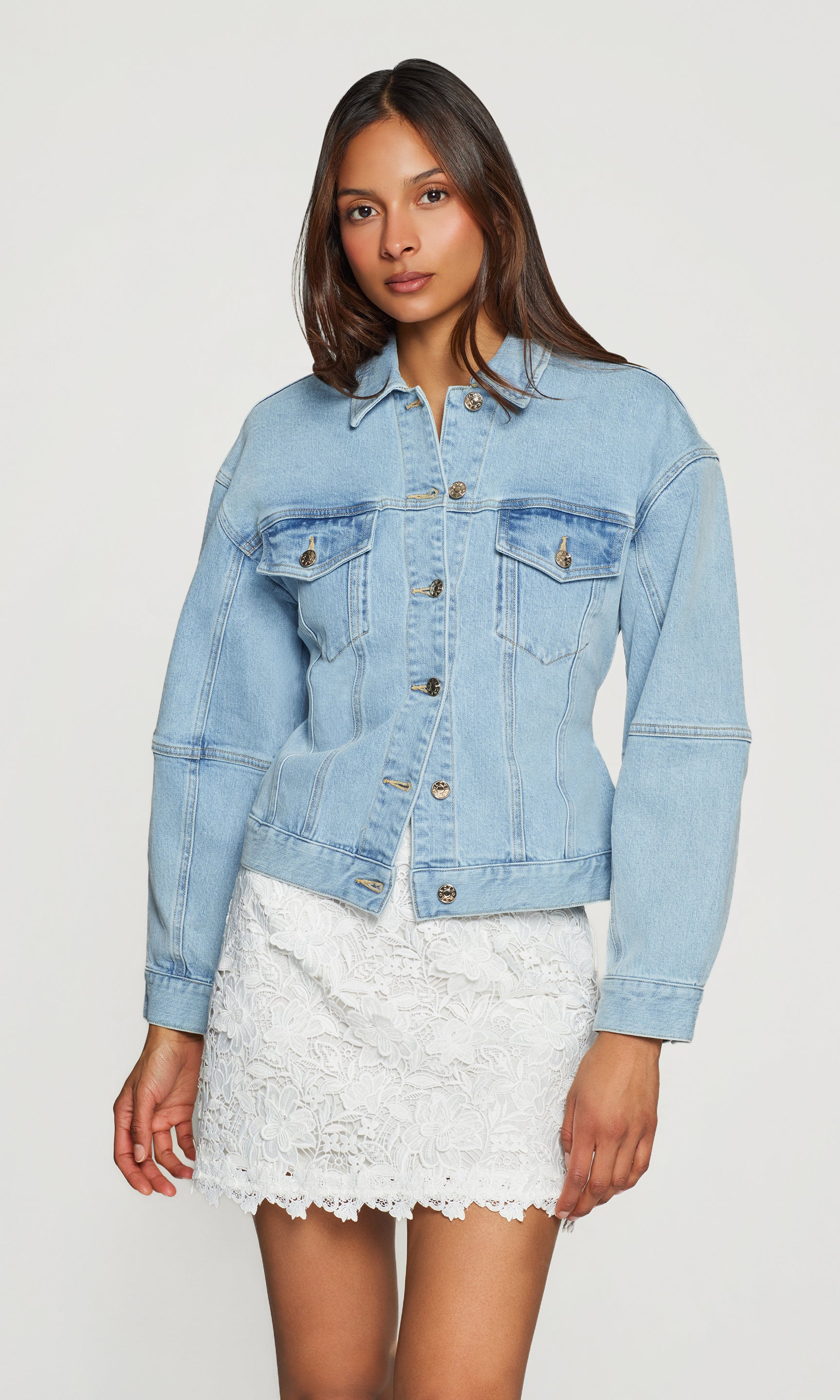 Woman wearing a light blue denim jacket over a white lace skirt on a white background
