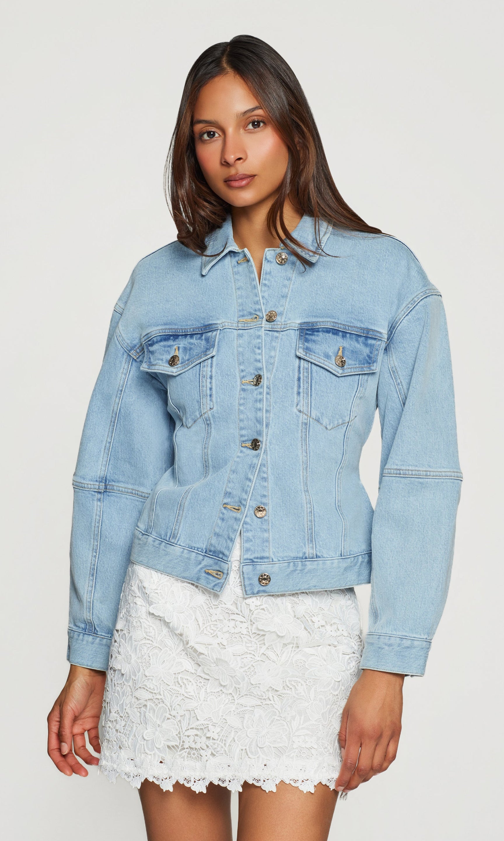 Woman wearing a light blue denim jacket over a white lace skirt on a white background