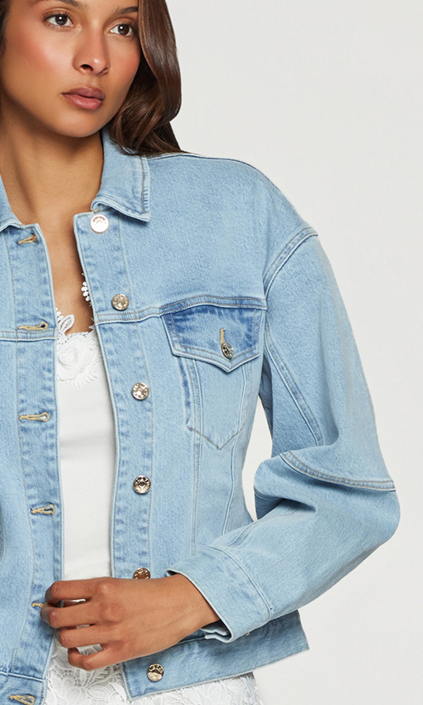 Close-up of woman wearing a light blue denim jacket on a plain background