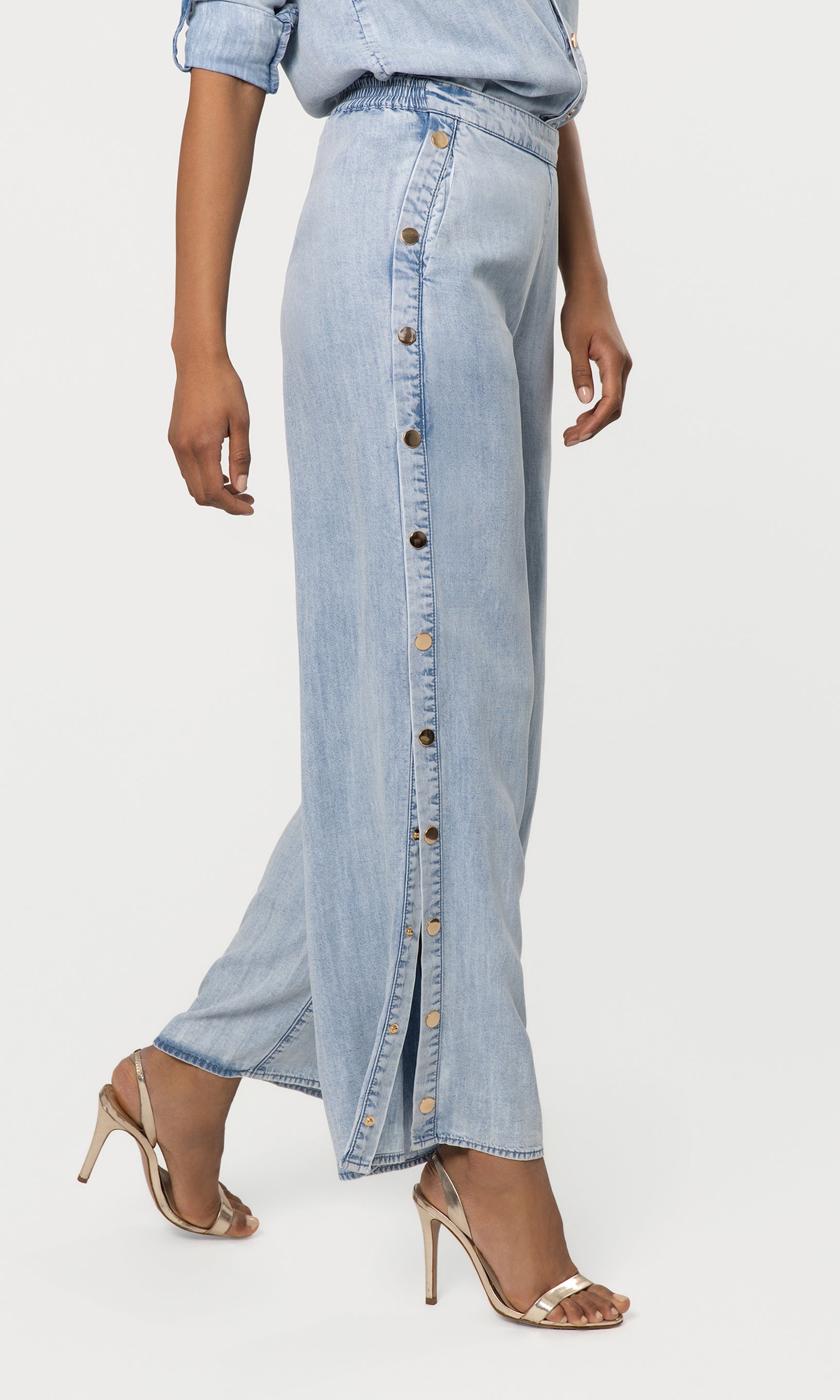Side view of light blue denim pant with button details worn by a person on a white background