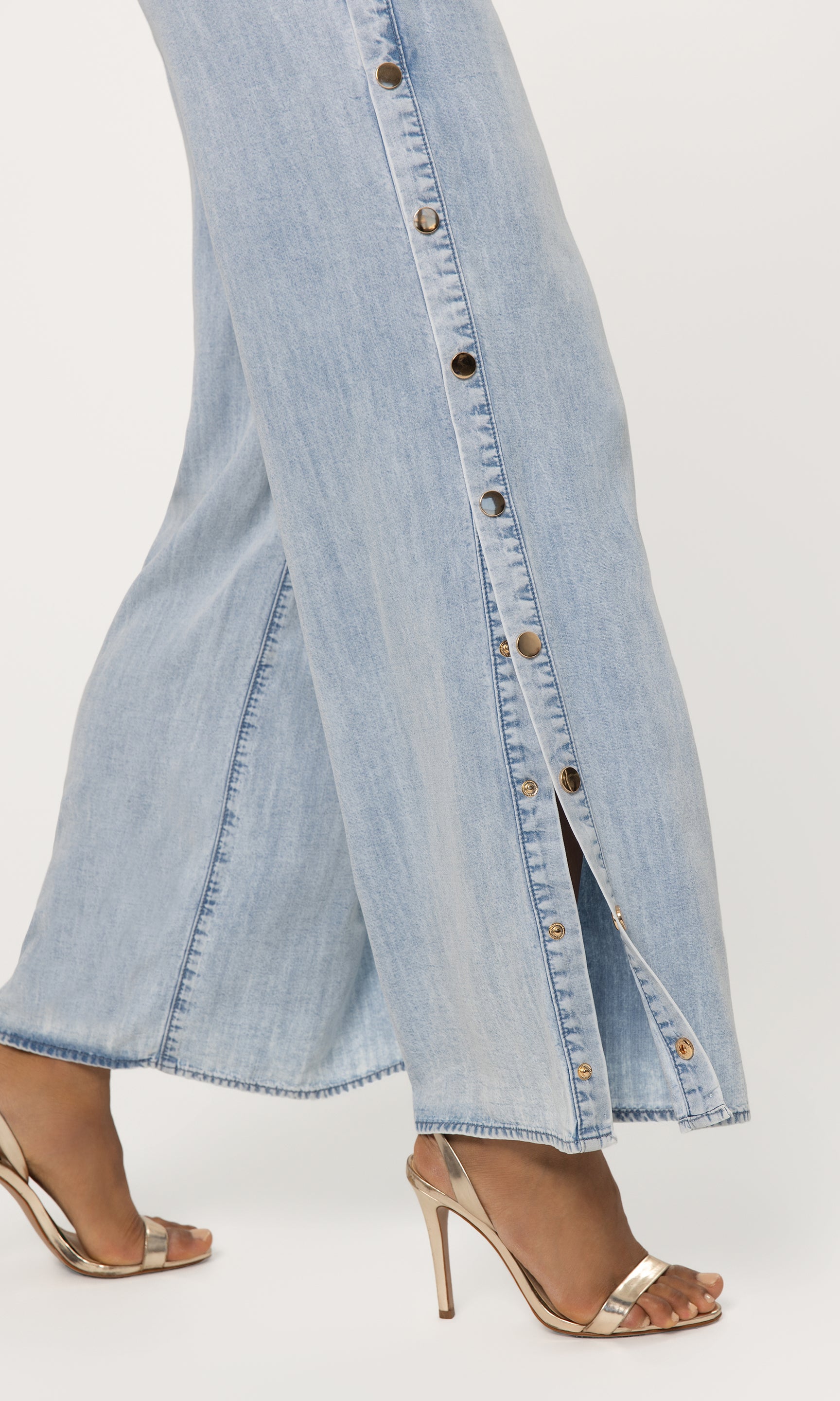 Close-up of light blue denim pant legs with button details on a white background