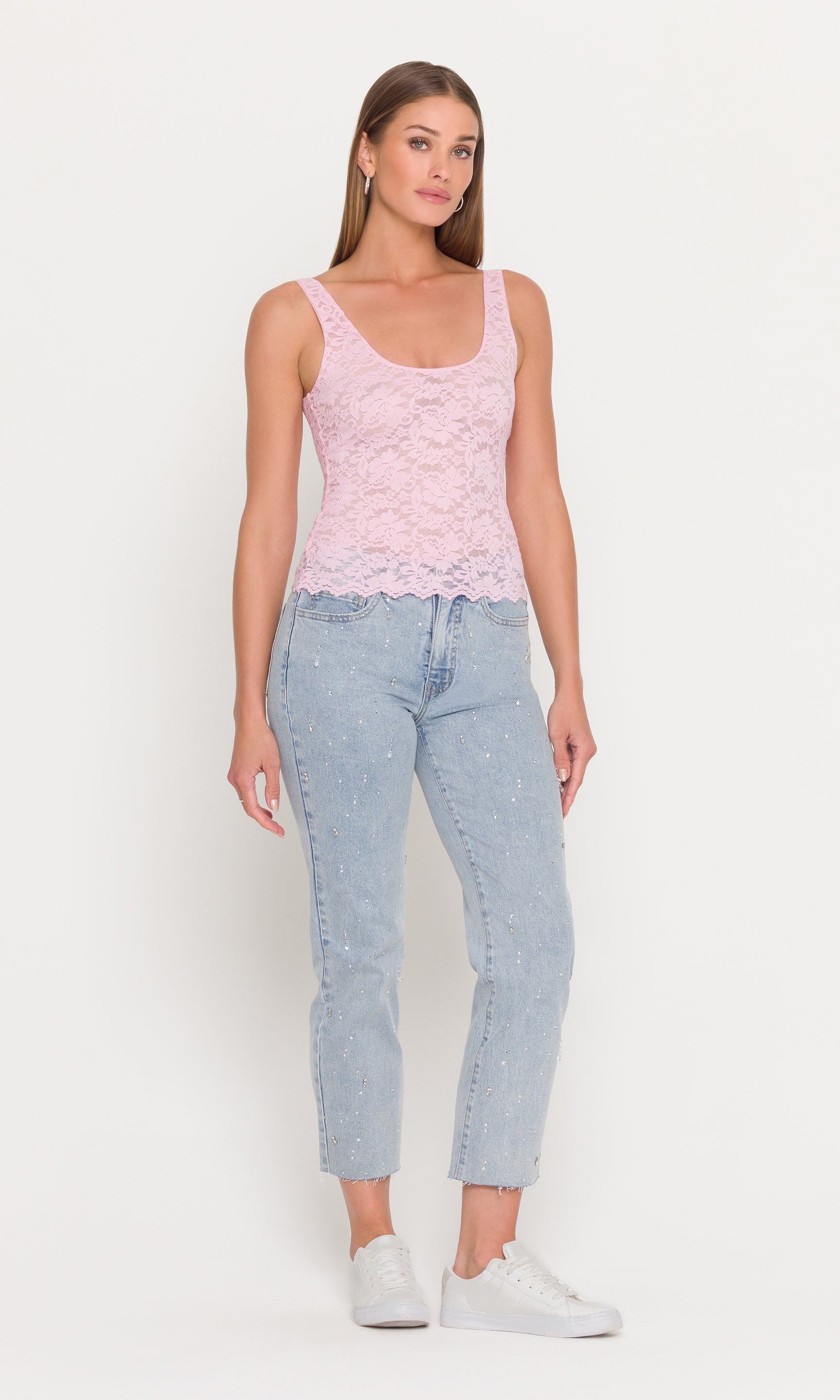 Woman wearing a pink lace top and light blue jeans on a white background