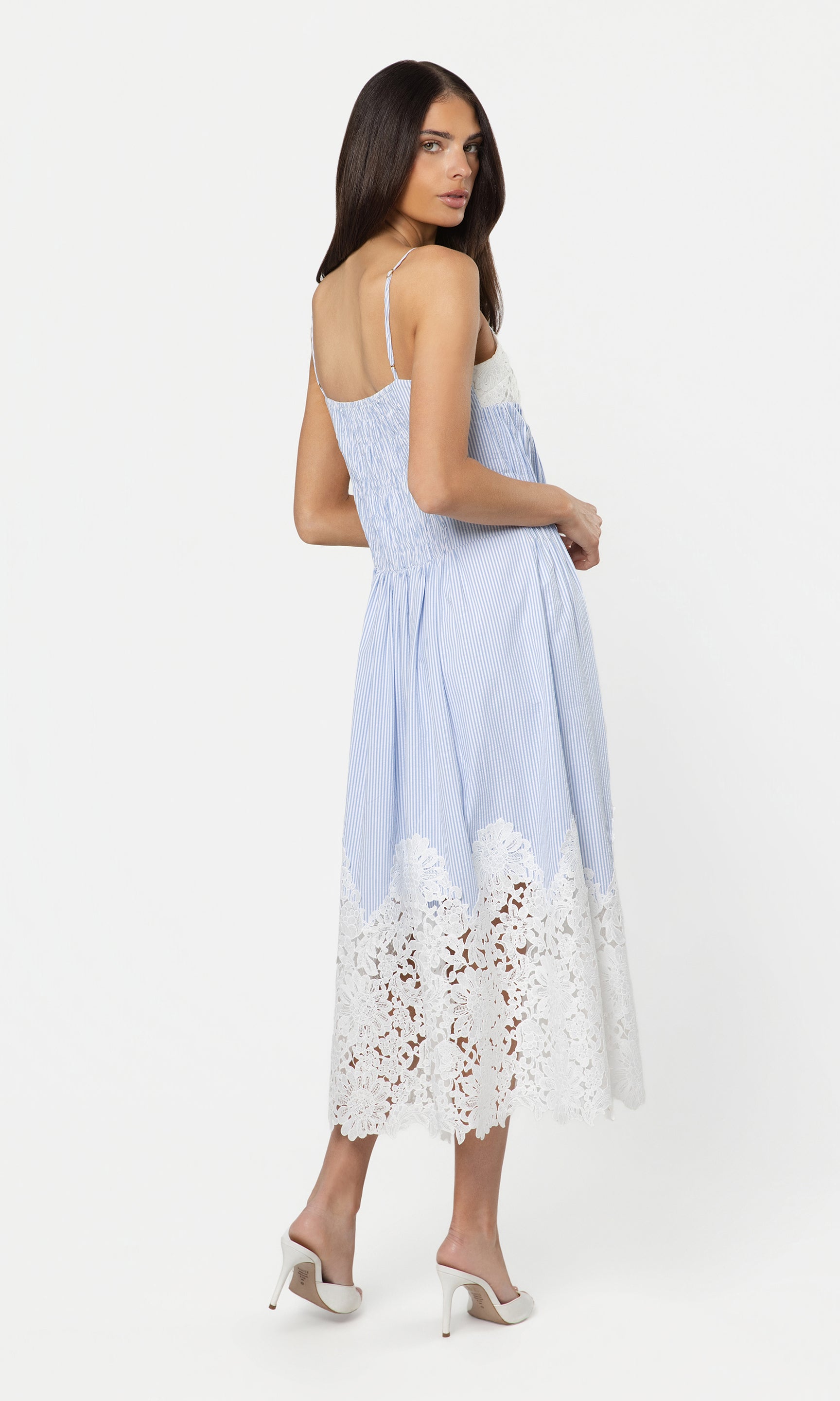 Back view of woman wearing a light blue dress with lace details on a white background