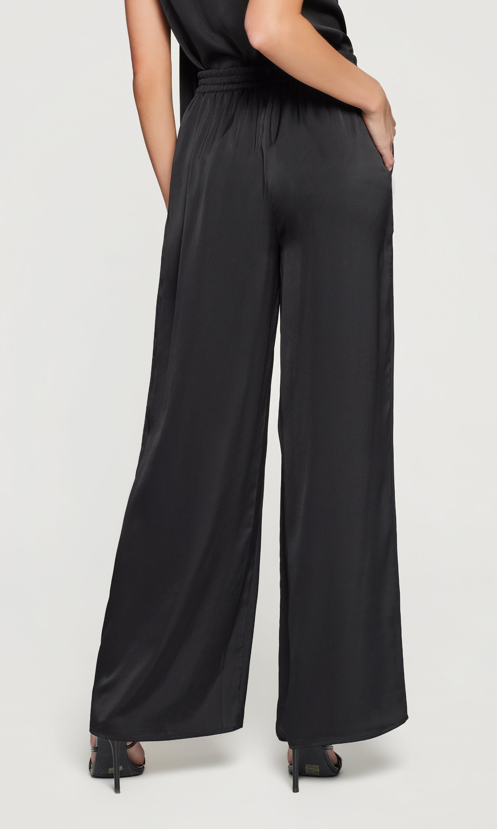 Back view of black pants worn by a person on a white background
