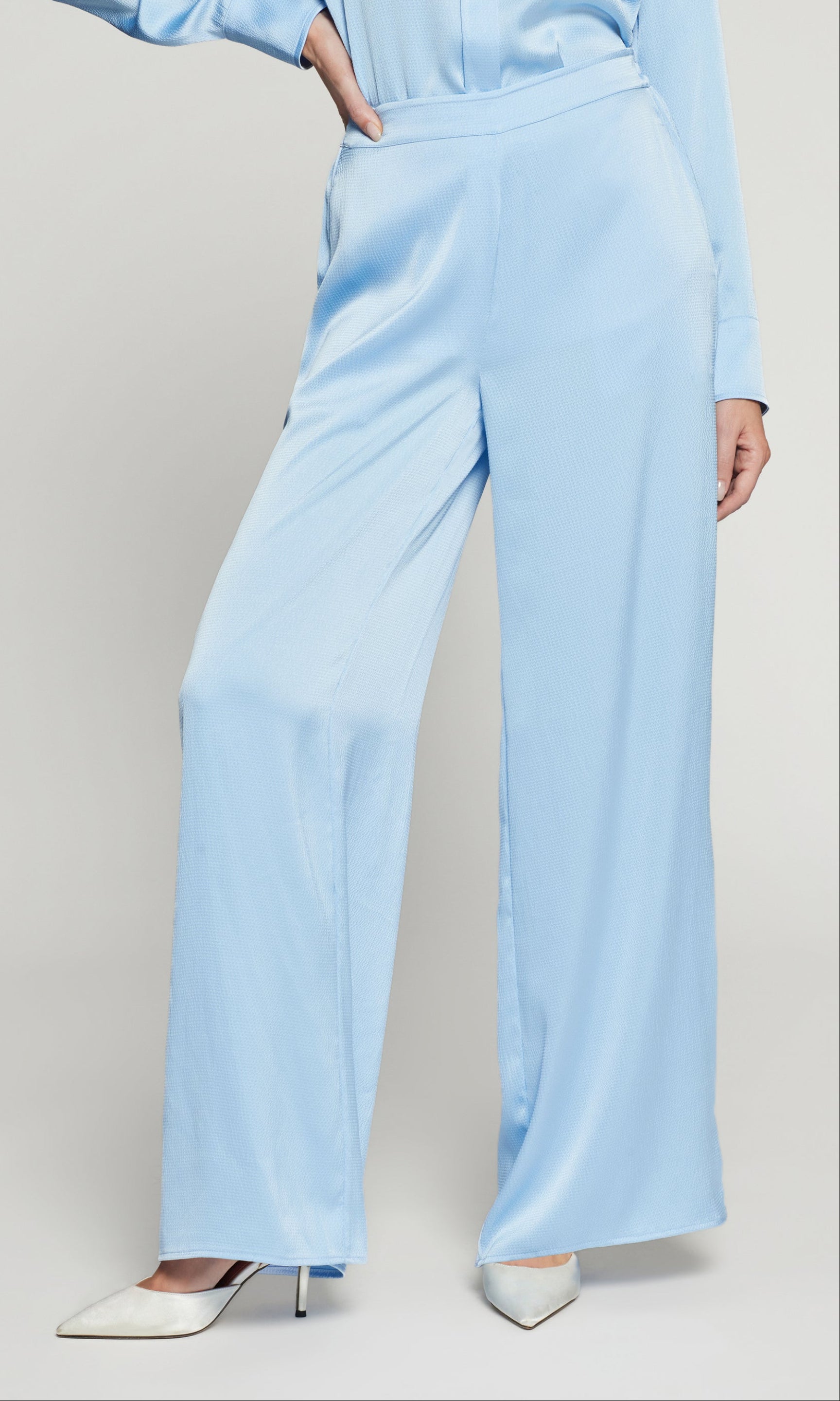 Person wearing a light blue outfit with wide-leg pants on a plain background