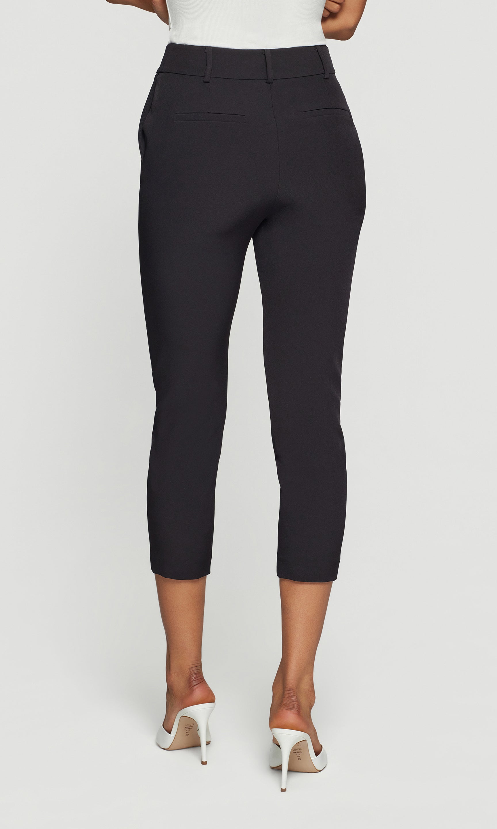 Back view of black capri pants worn by a person on a white background