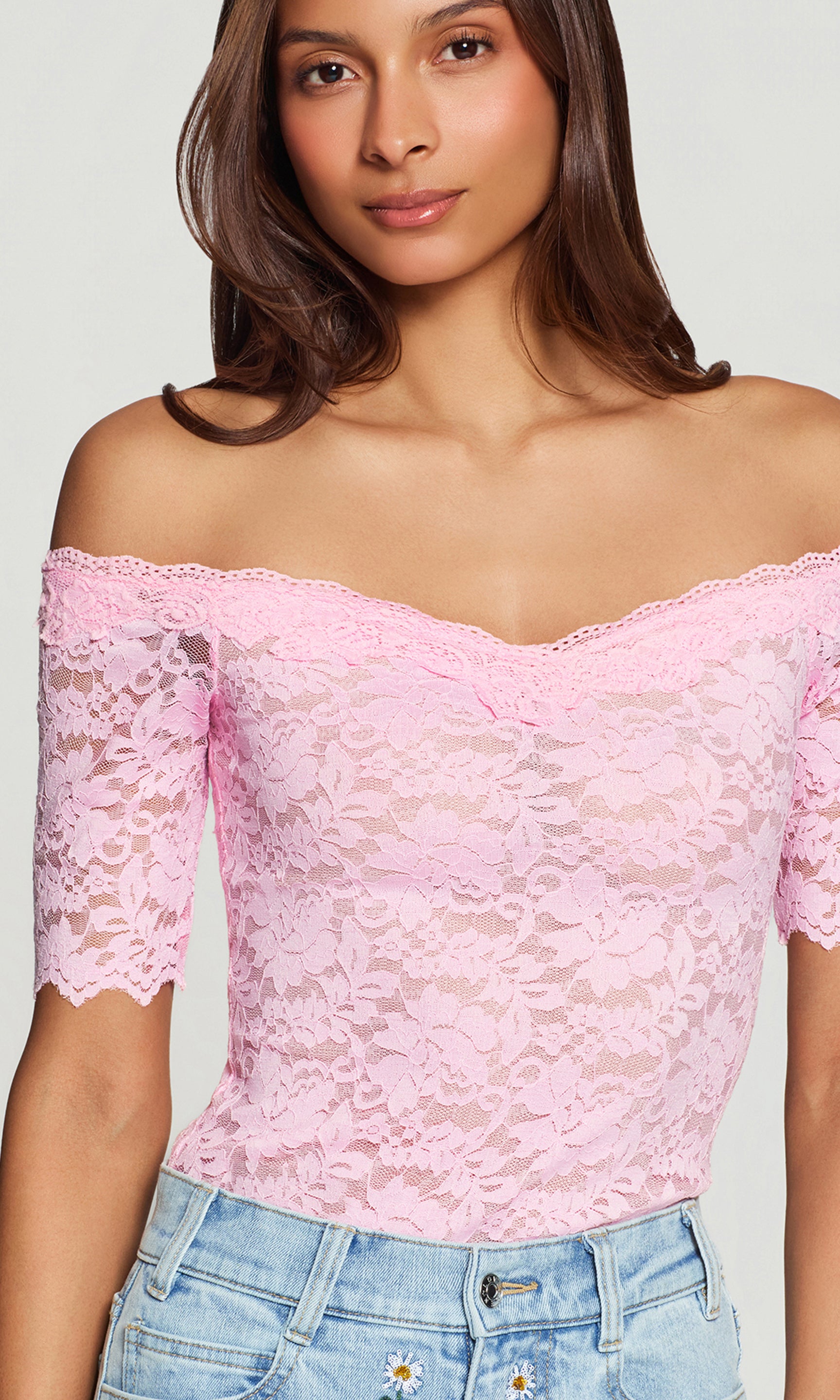 Close-up of woman wearing a pink lace top with denim bottoms on a white background