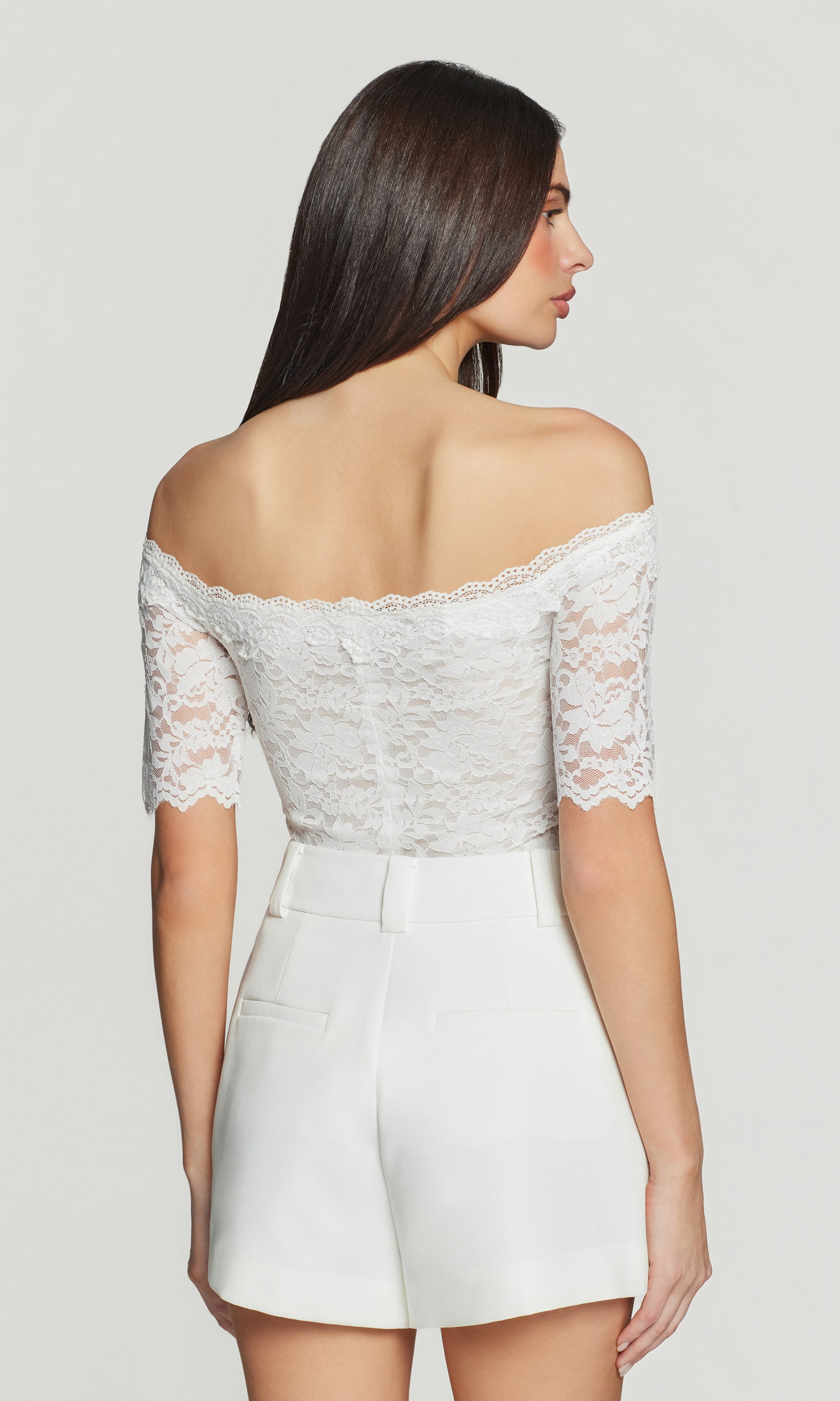 Back view of woman wearing a white lace top and shorts set on a plain background