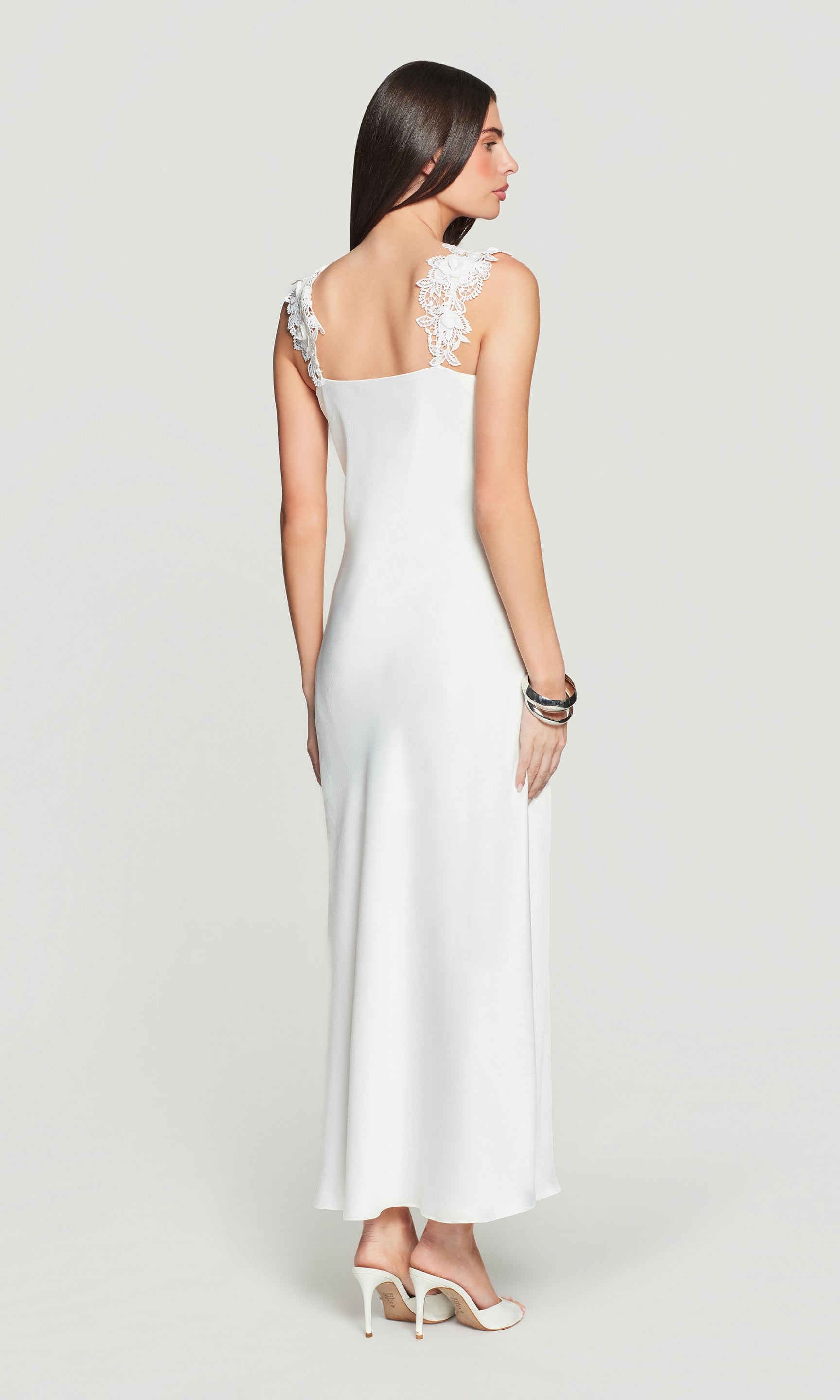 Back view of woman wearing a white dress with lace straps on a light gray background