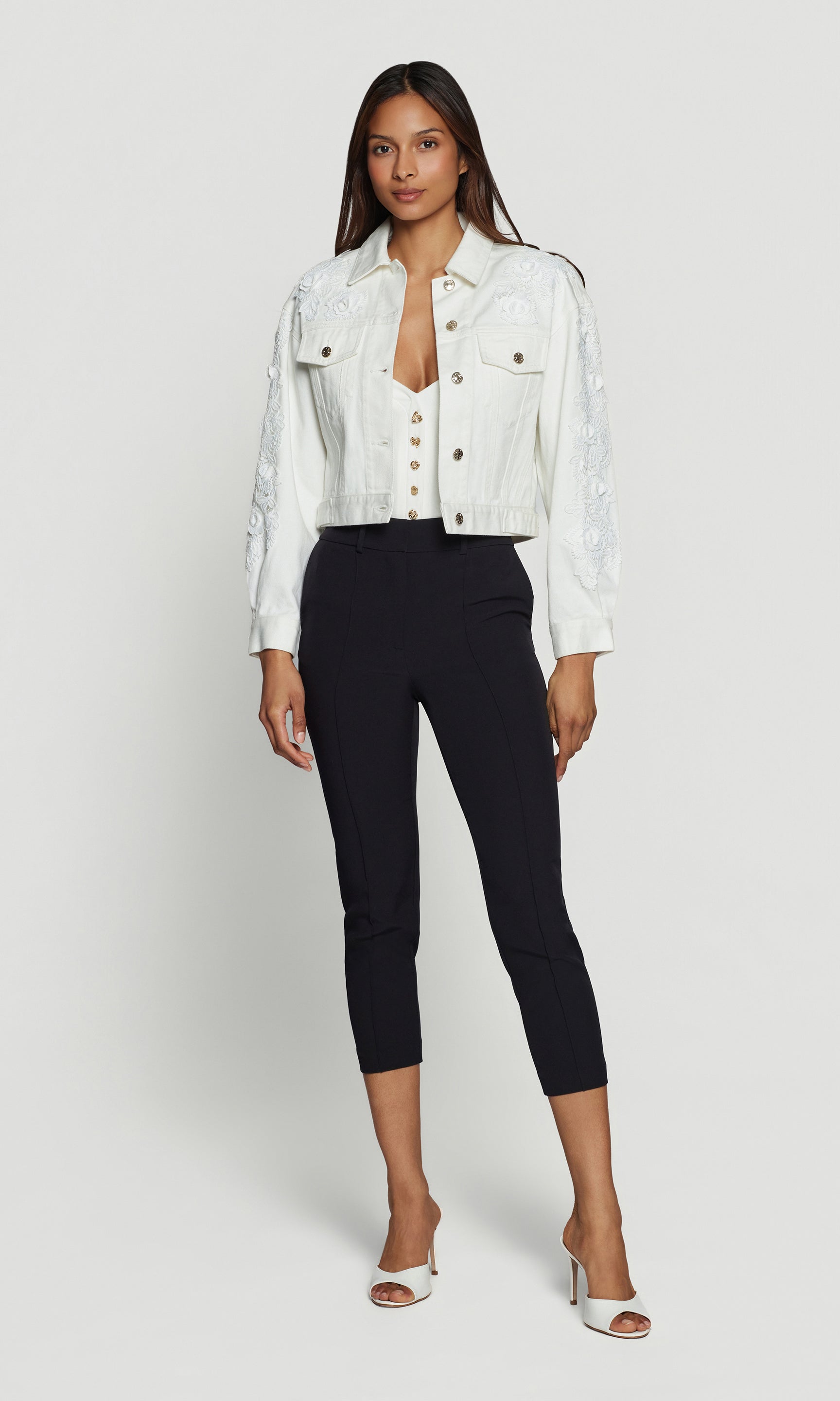 Woman wearing a white denim jacket and black pants on a white background